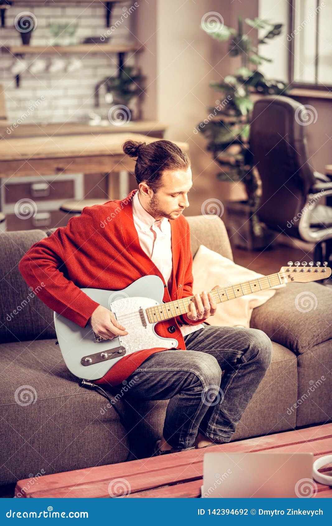 bearded instrumentalist sitting on sofa and playing the guitar