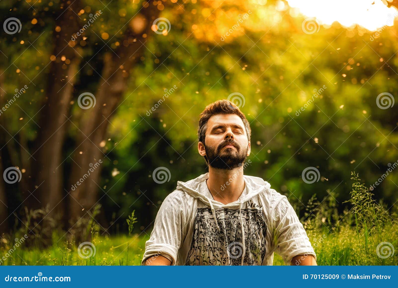 a bearded man is meditating on green grass in the park
