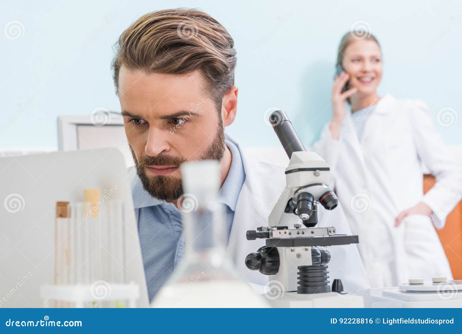 Bearded Scientist Working with Microscope and Laptop in Laboratory