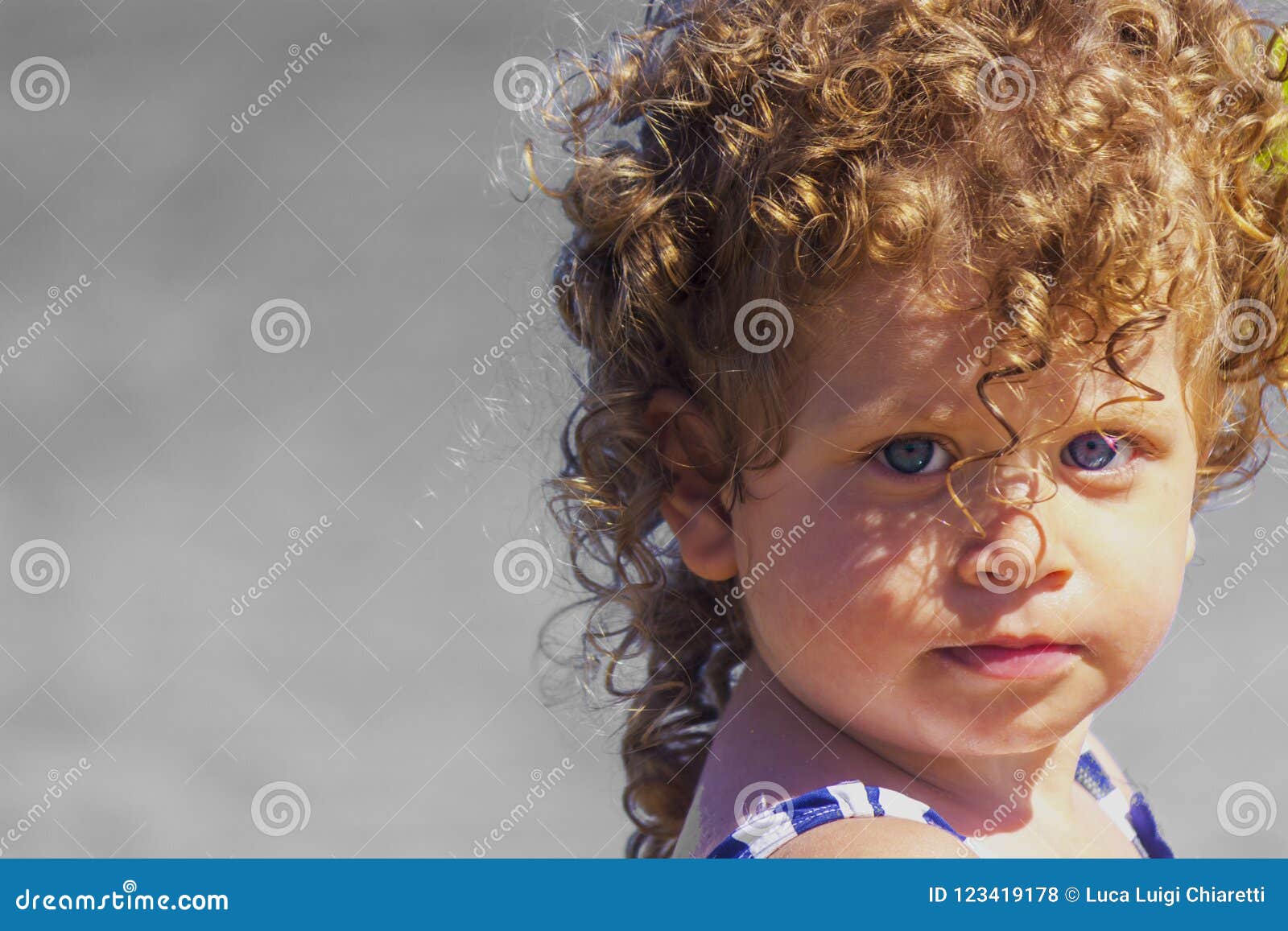 Beau bébé sur la plage. Une belle petite femme avec des yeux bleus et des cheveux blonds bouclés