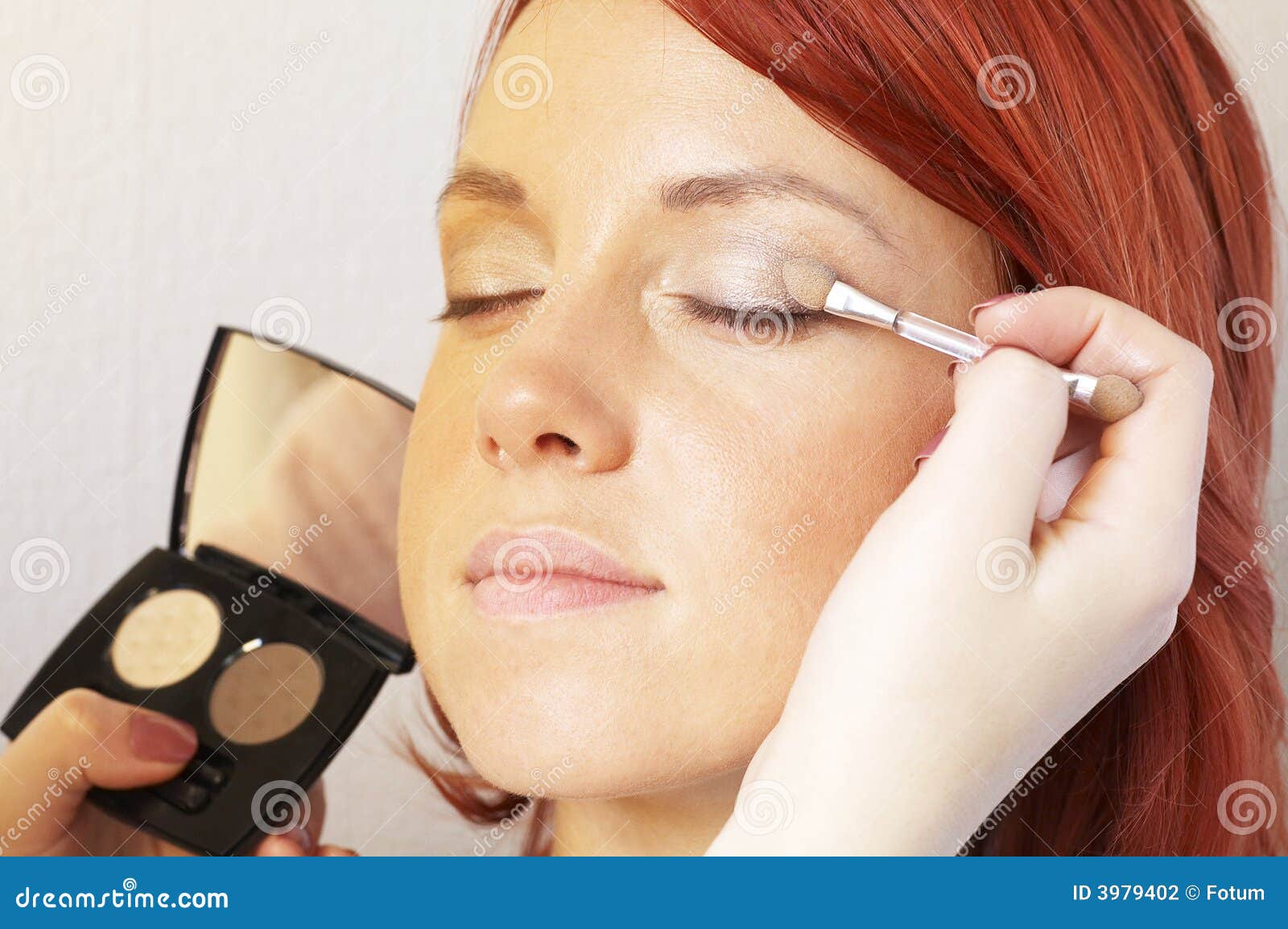 beautician is doing make-up to red-haired girl
