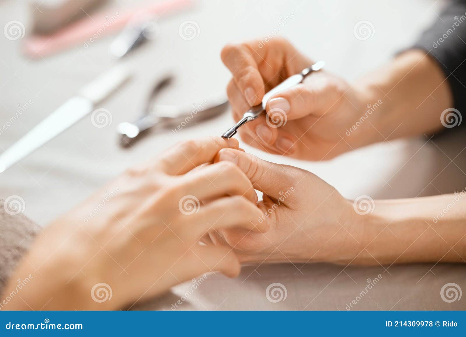 beautician using cuticle pusher on woman hand