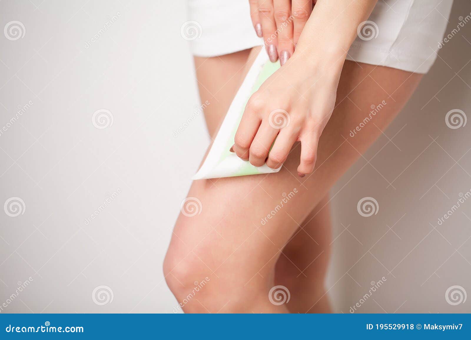 beautician waxing a woman`s leg applying wax strip