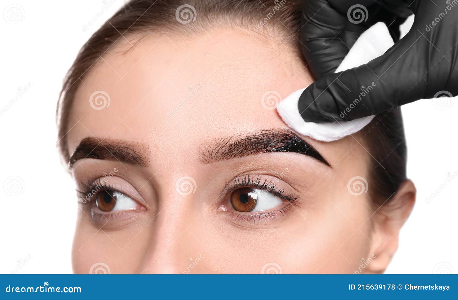 beautician wiping tint from woman`s eyebrows on white background, closeup