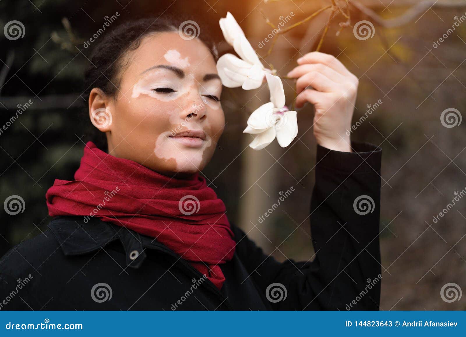 beautiful african girl with vitiligo standing on the street sniffs spring flowers