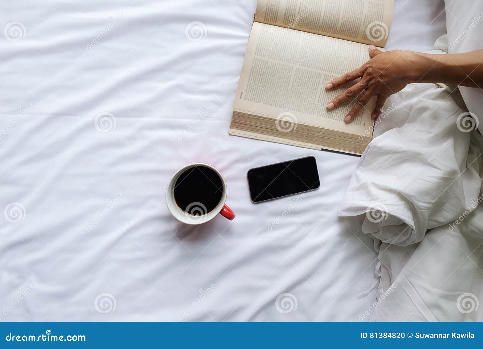 beautiful asian female sitting on the bed with a cup of coffee and reading a book