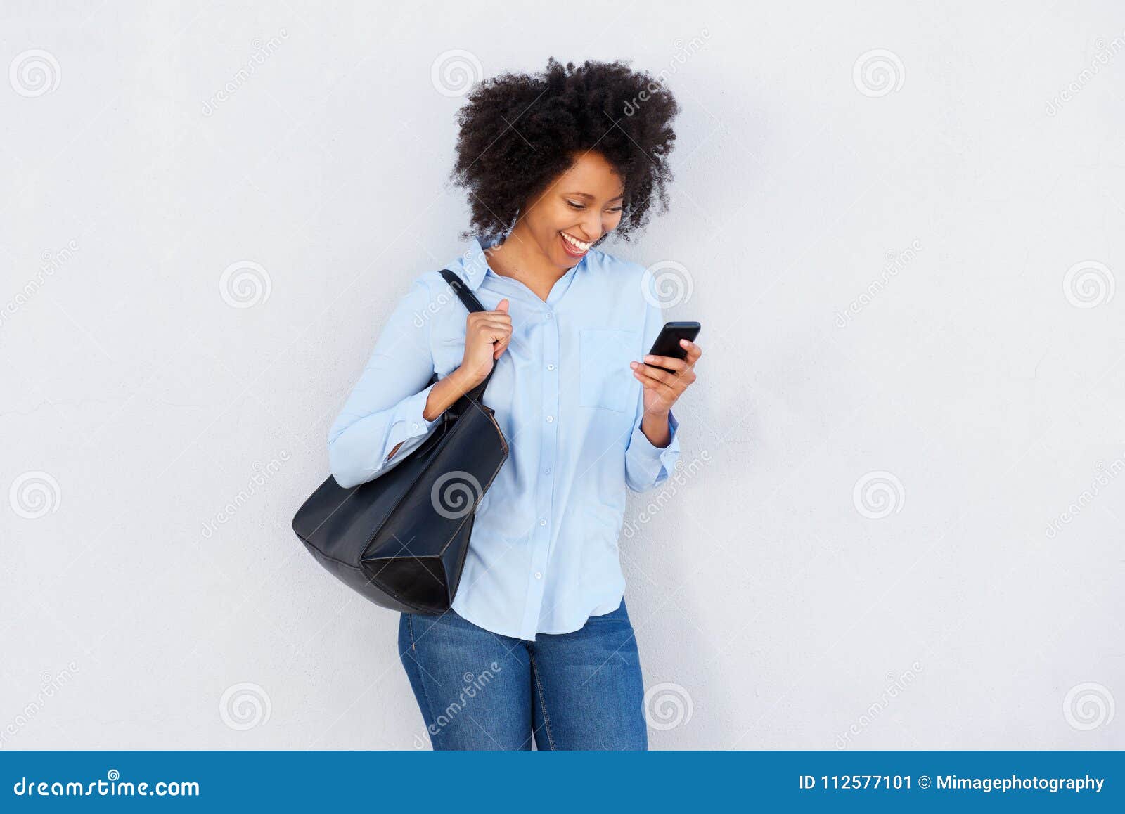 beautiful black woman with purse looking at cellphone and laughing