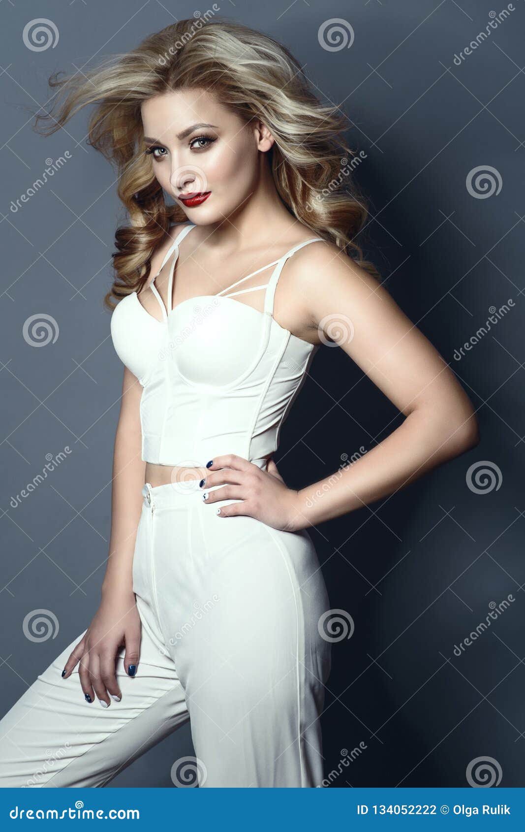 beautiful blond model with perfect make up and wavy hairstyle wearing white high waisted pants and corset strapped top