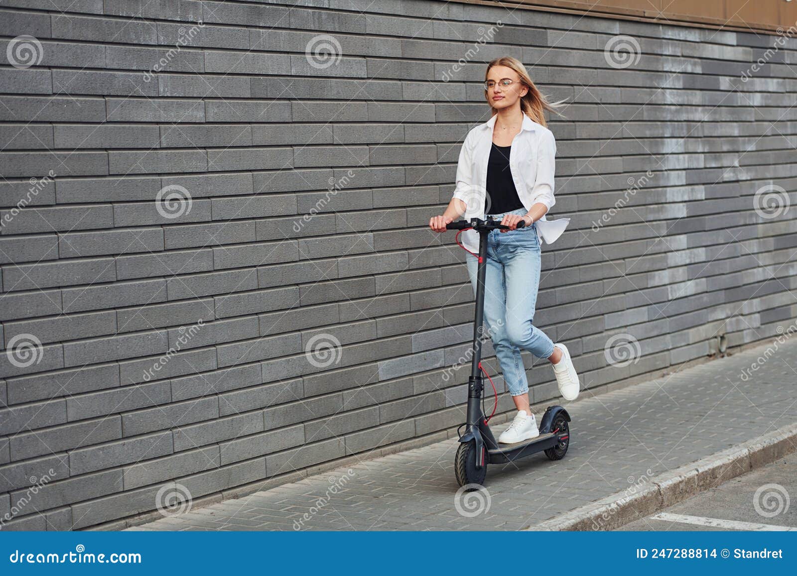 Beautiful Blonde In Casual Clothes Riding Electric Schooter Outdoors At Sunny Daytime Stock
