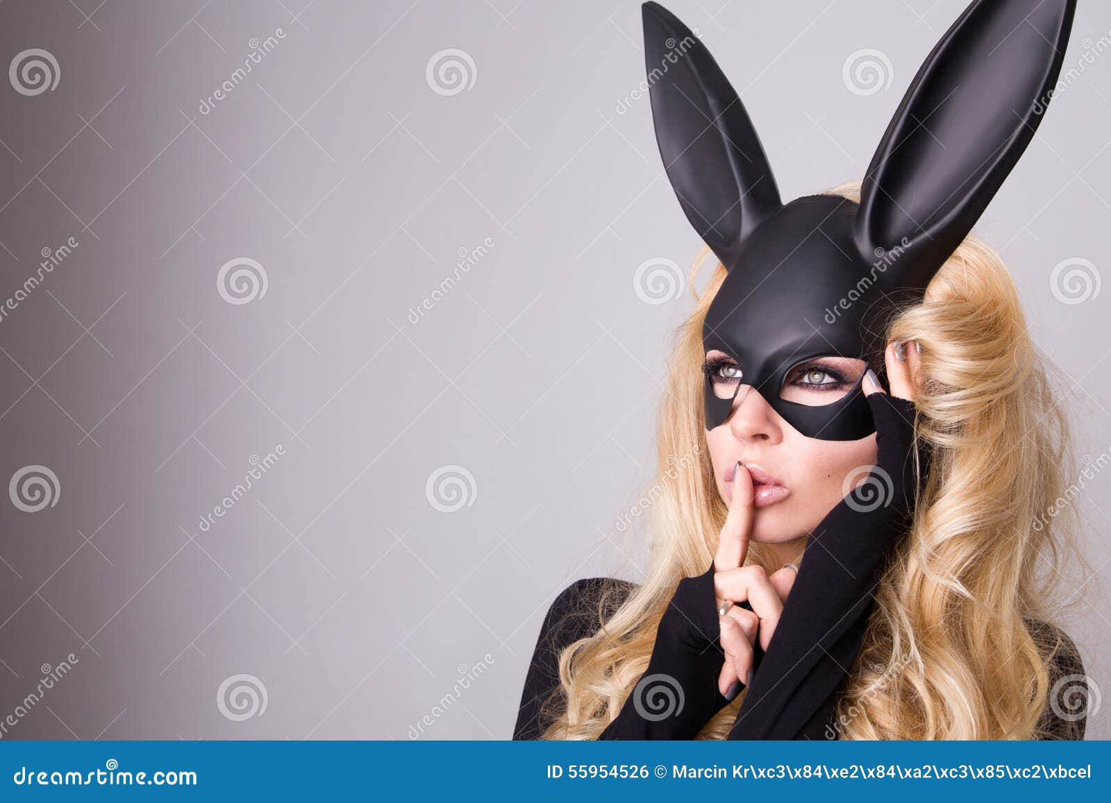 beautiful blonde-haired young woman in carnival mask ballroom rabbit with long ears sensual in a black dress, standing defian