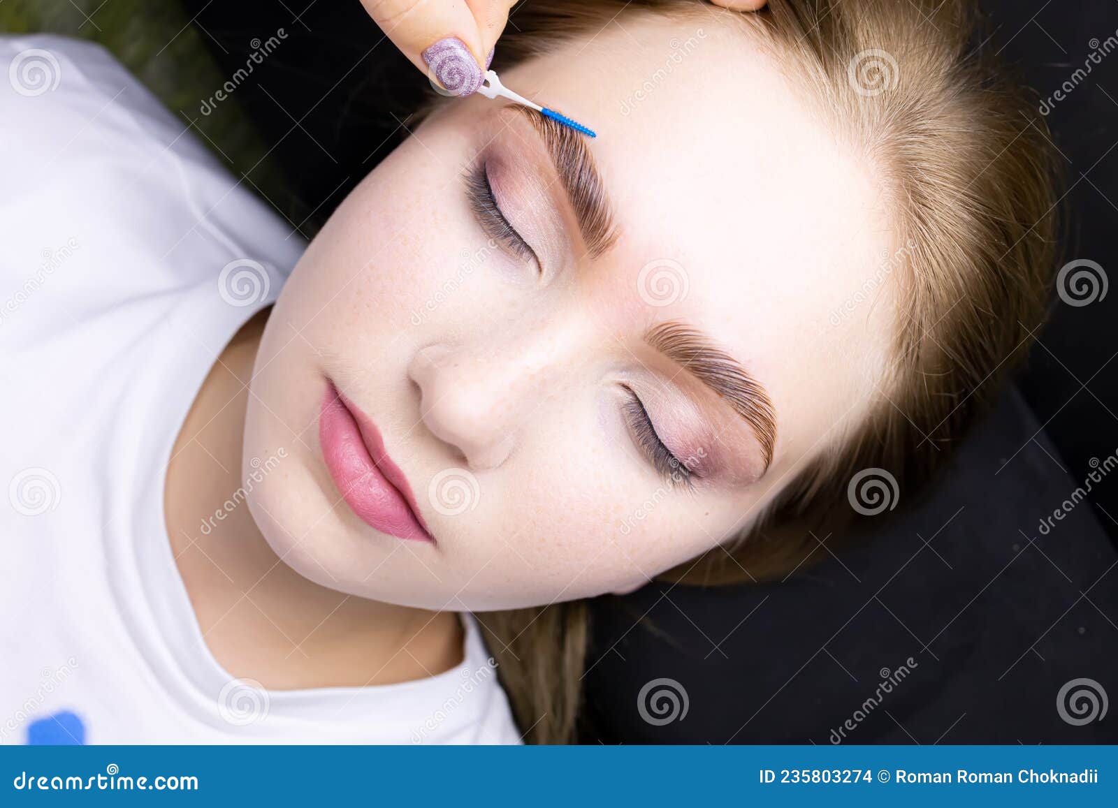 a beautiful blonde model lies after the eyebrow lamination procedure, the master combs the eyebrow hairs