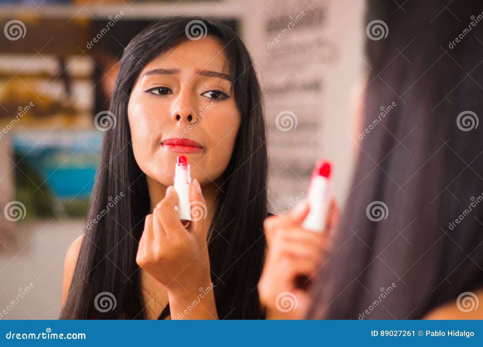 beautiful brunette applying make up while smiling happily, seen from behind and face reflecting in mirror