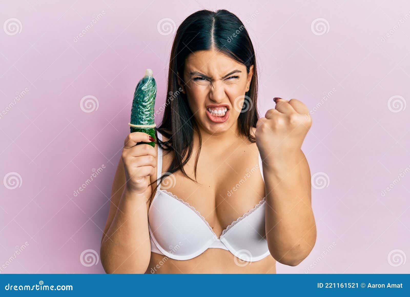 Beautiful Brunette Woman Holding Condom on Cucumber for Sex Education Annoyed and Frustrated Shouting with Anger, Yelling Crazy Stock Image photo