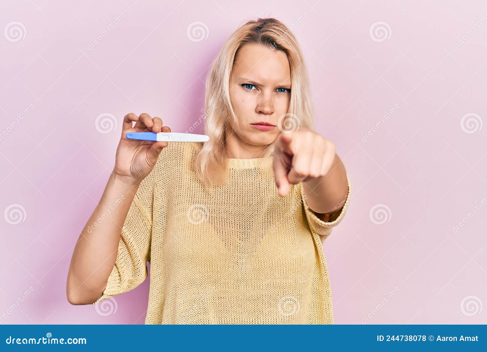 Beautiful Caucasian Blonde Woman Holding Pregnancy Test Result Pointing With Finger To The
