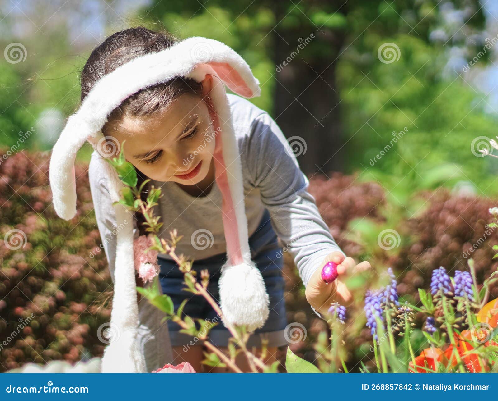 a beautiful caucasian little girl in a bunny ear headband, a t-shirt and shorts found and takes out a chocolate easter