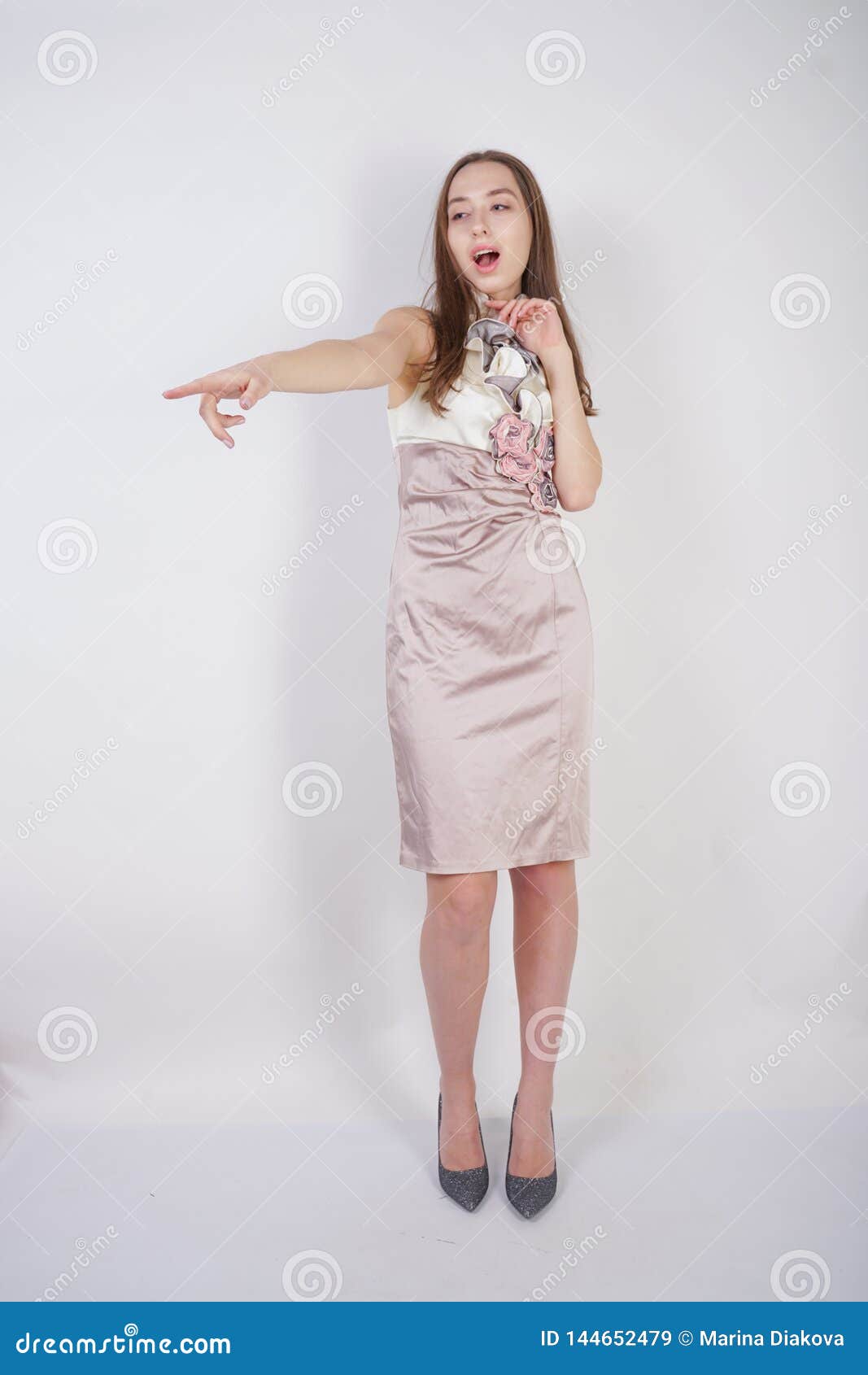 beautiful caucasian teen girl stands in a short evening dress and mocks the interlocutor, humiliating, on a white background in th