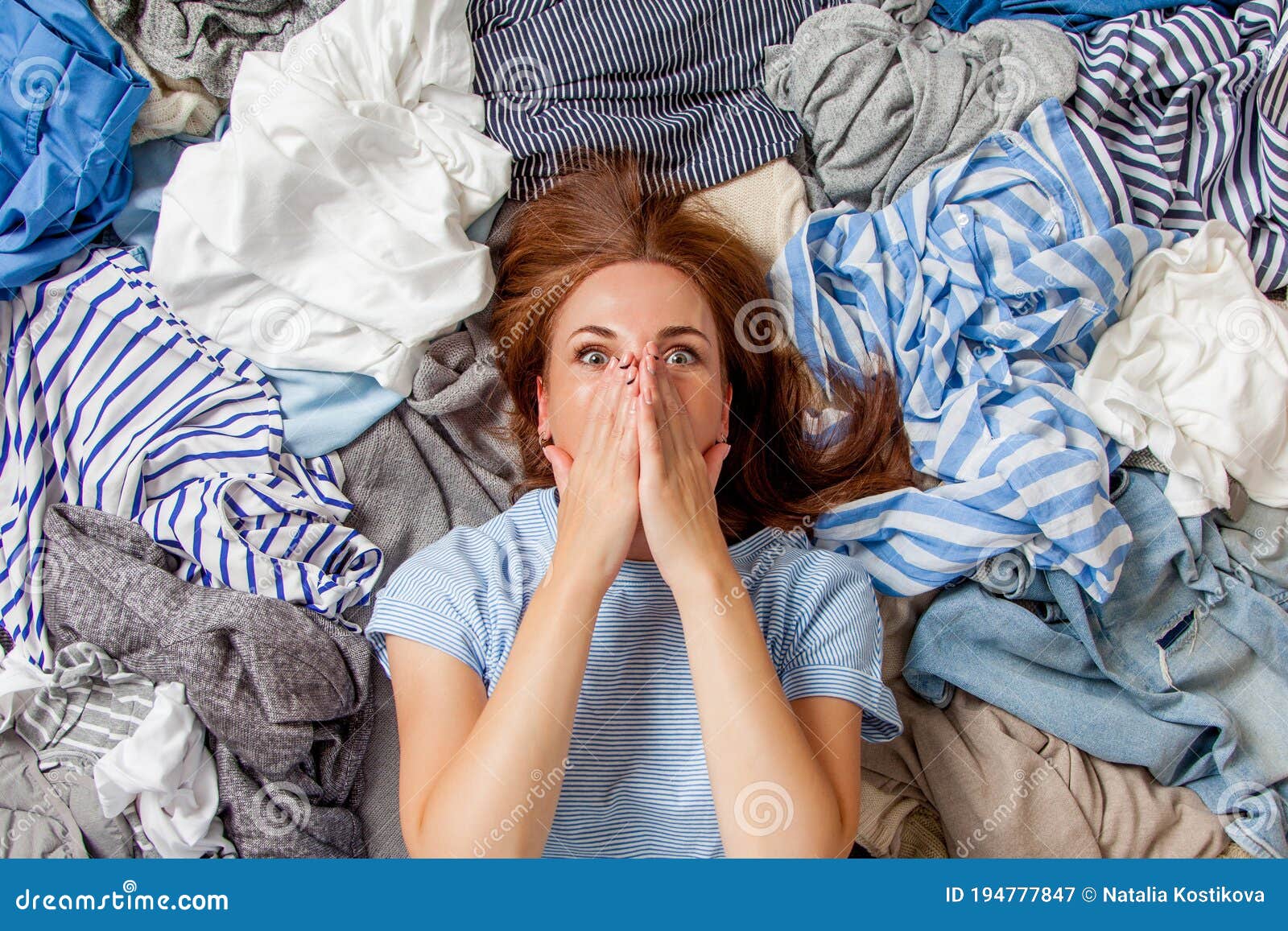 beautiful caucasian woman smiling and lying down with clutter clothes on the floor.