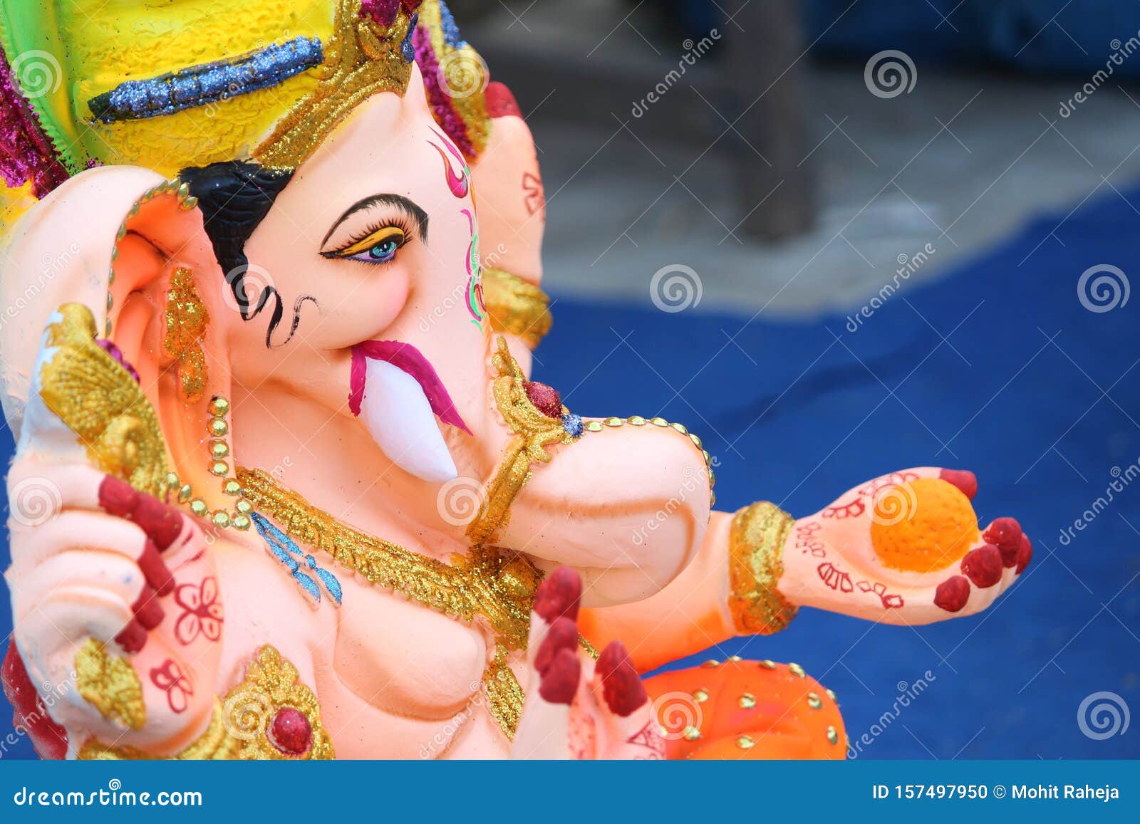 a beautiful clay statue/idol of an indian god lord ganesha decorated with colorful drapery and marigold garland