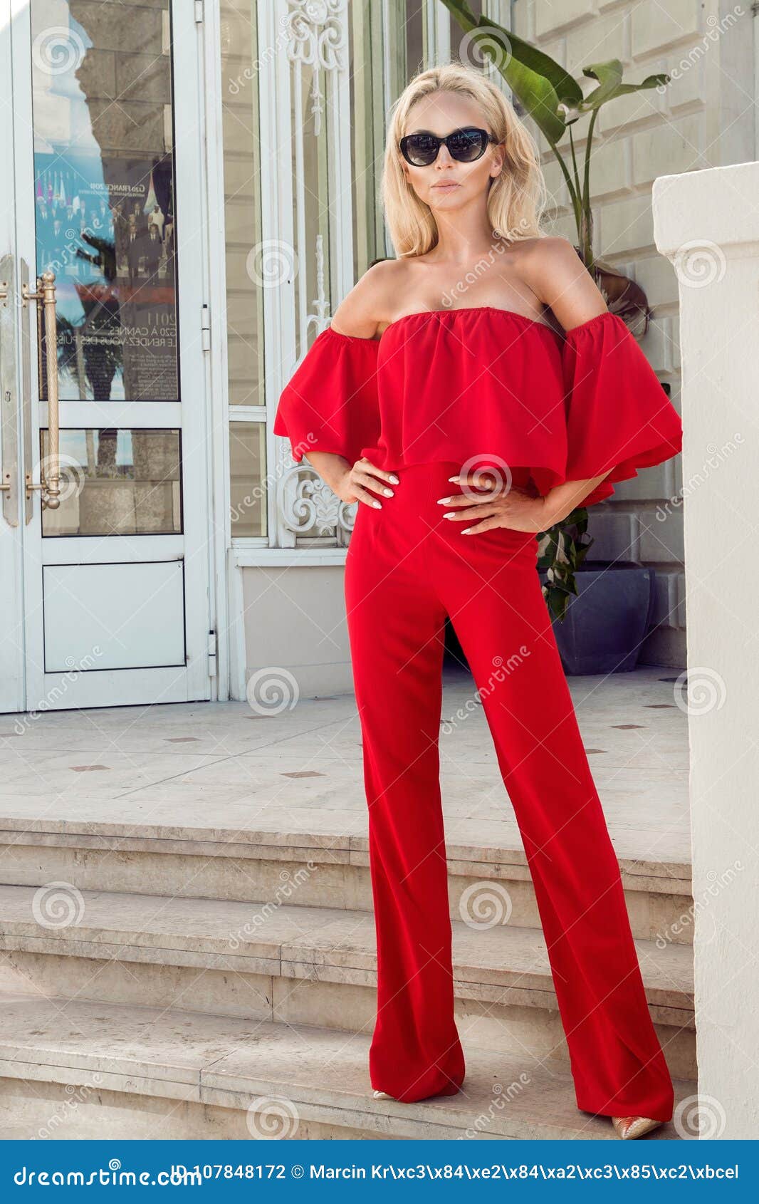 beautiful elegant female fashion model in red dress standing in front of the luxury hotels and boutiques
