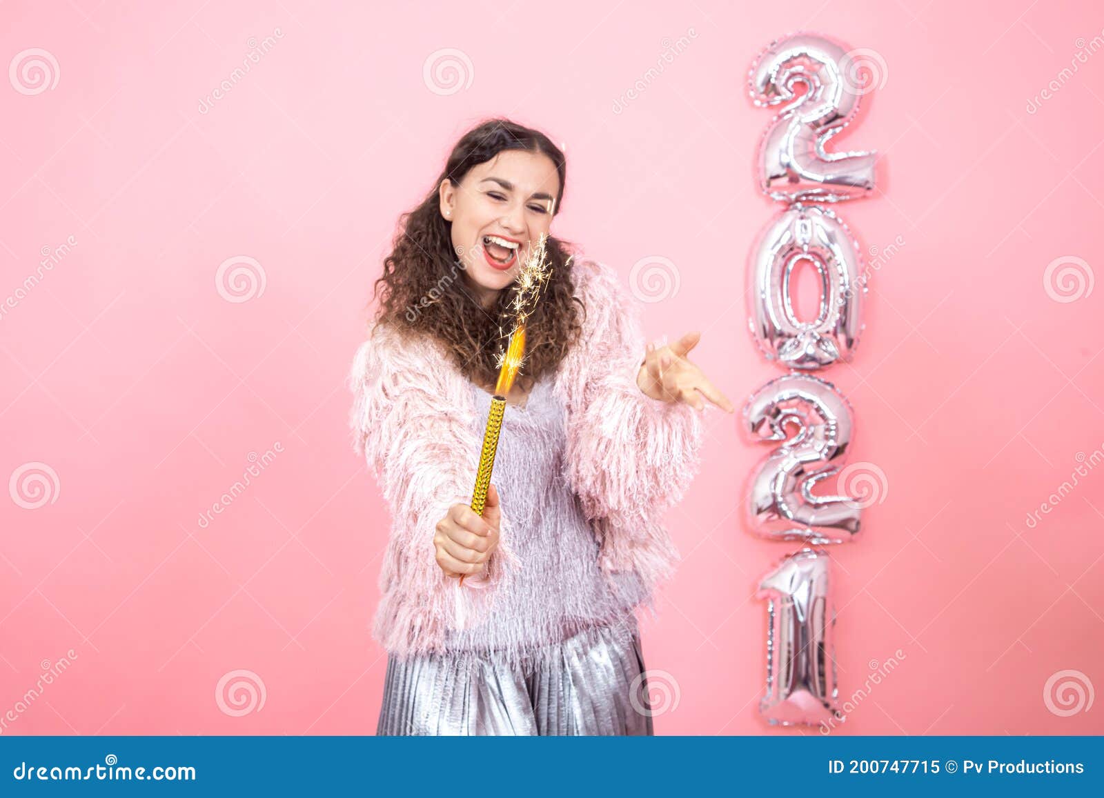 young woman on a pink background with silver ballons in the form of the numbers 2021