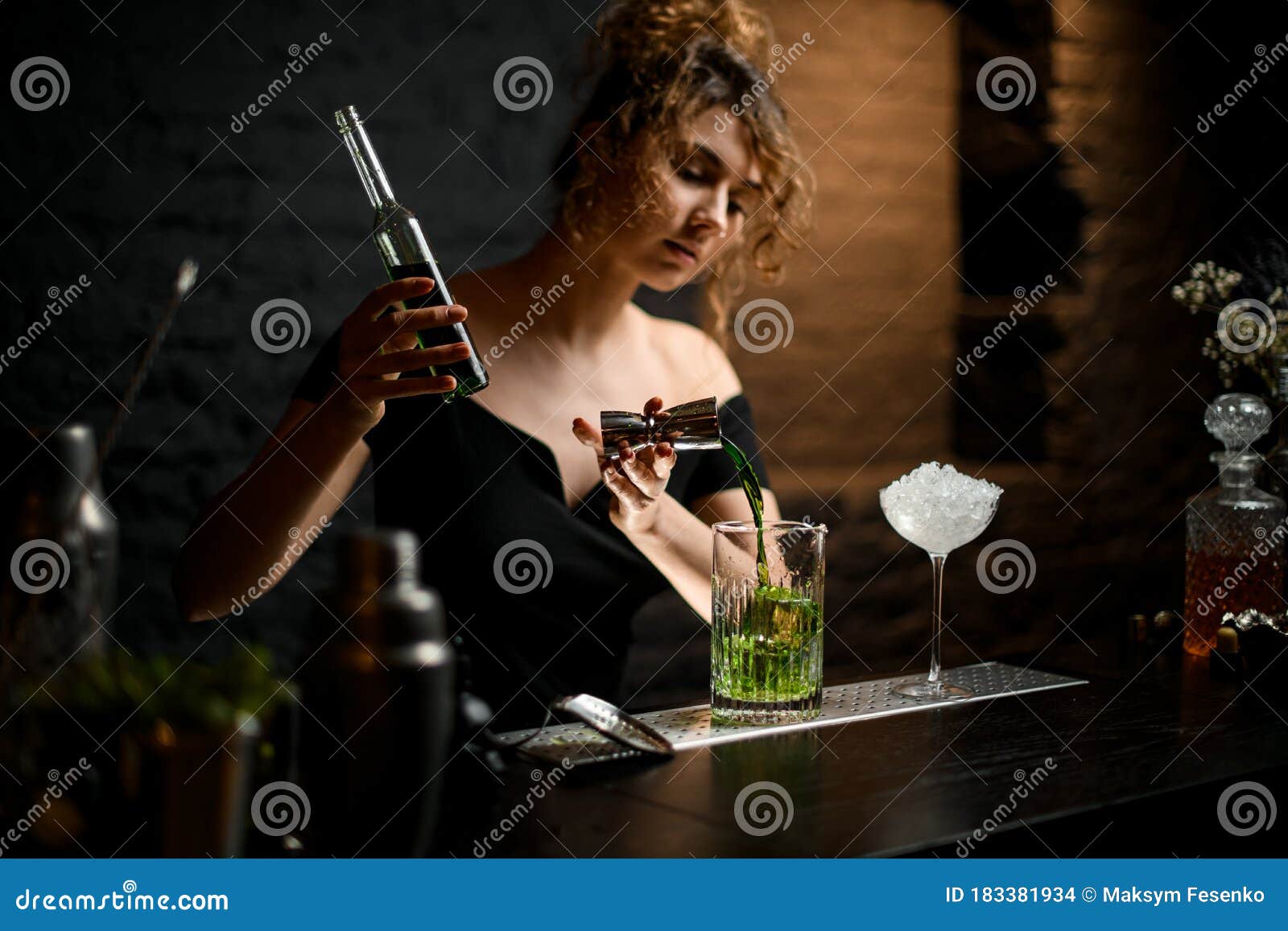 beautiful female bartender professionally pours blue drink from jigger into cup.