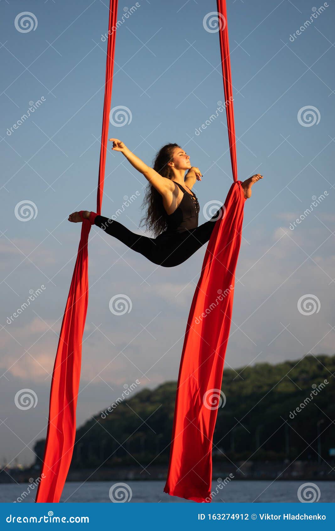Beautiful And Flexible Female Circus Artist Dancing With Aerial Silk With Sky And River