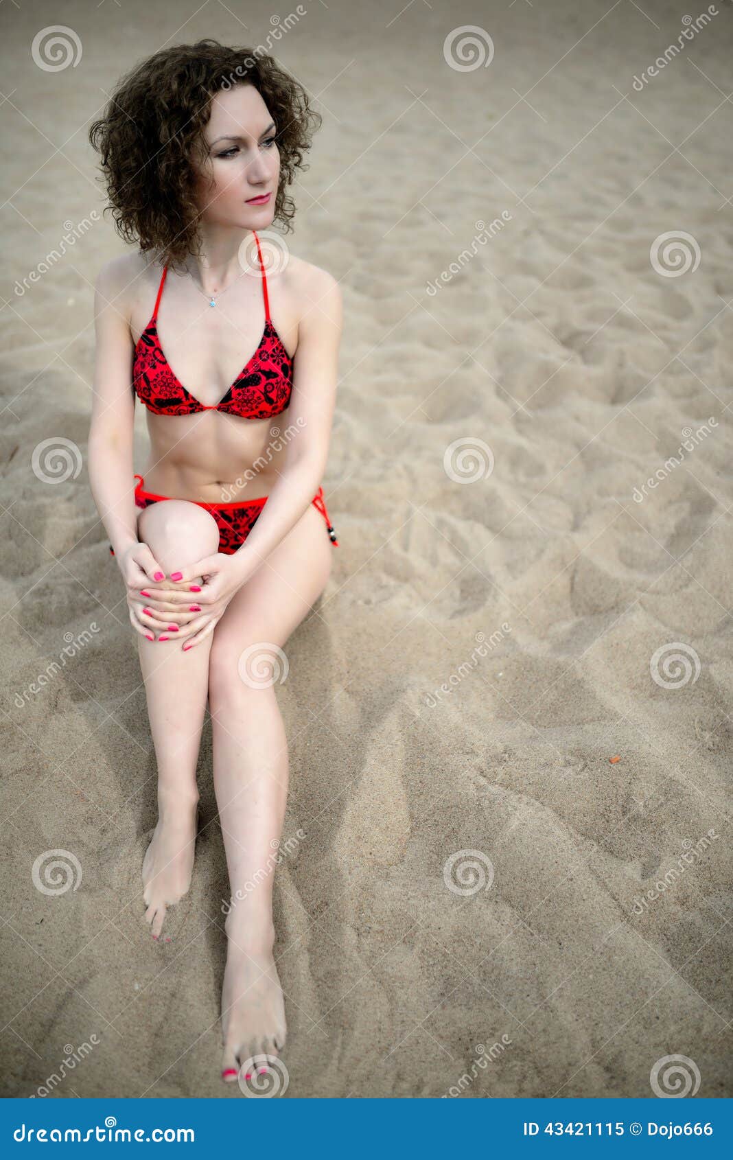The Beautiful Girl With A Curly Hair In A Red Bikini Sit On A Beach