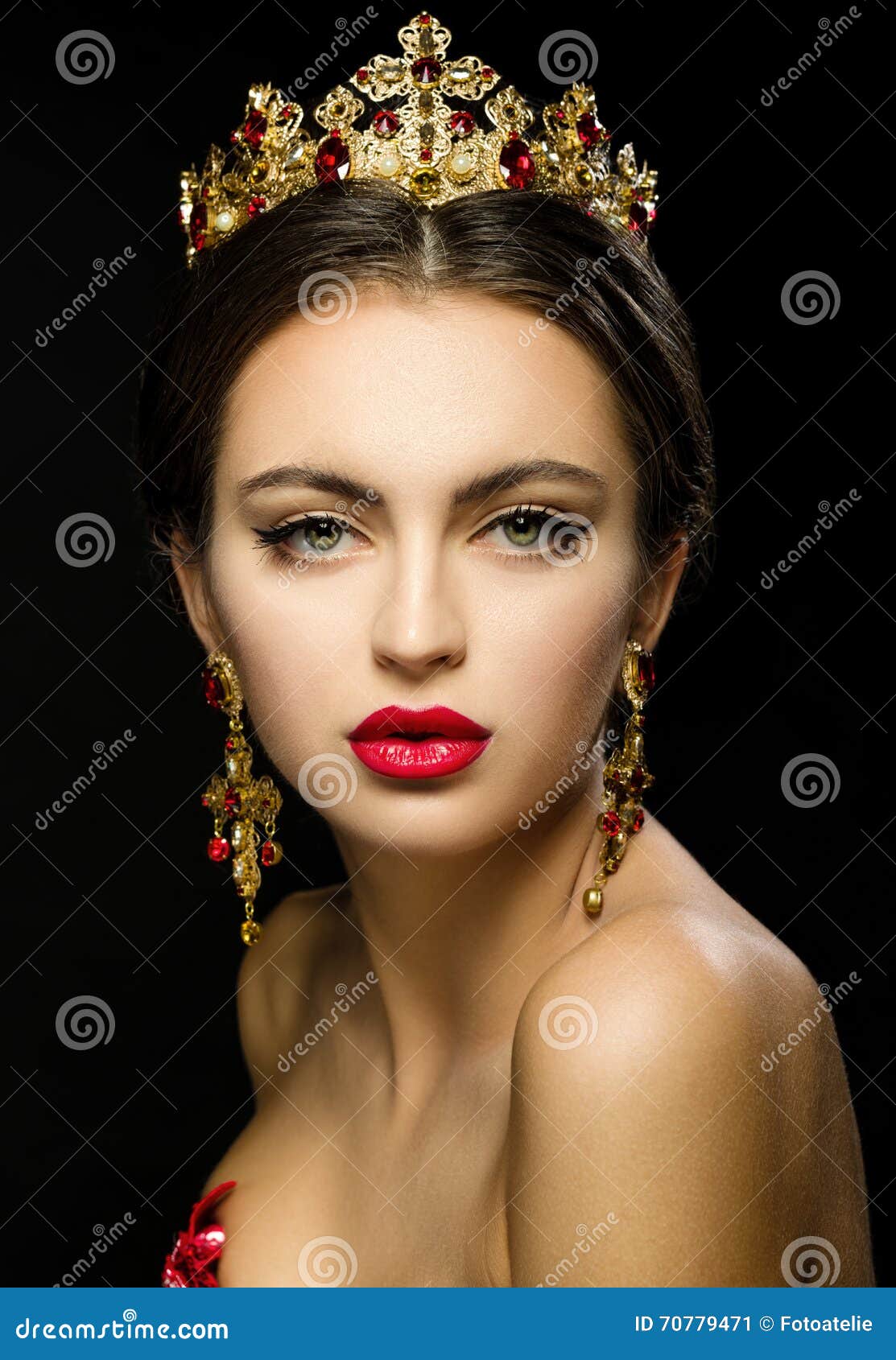 Close-up Portrait of Beautiful girl in a golden crown and earrings on a dark background. Red dress and red lipstick. Ring in the heart shape.