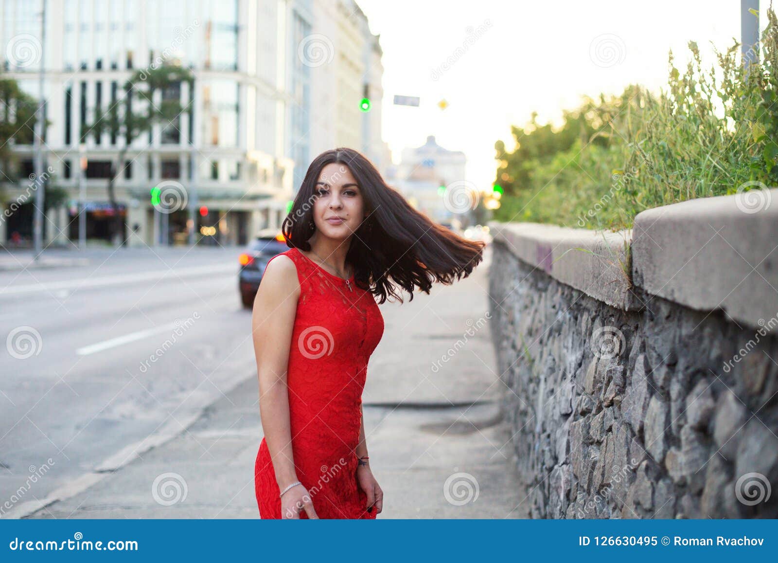 Beautiful Girl In A Red Dress Is Standing Near Of The Roadway Stock