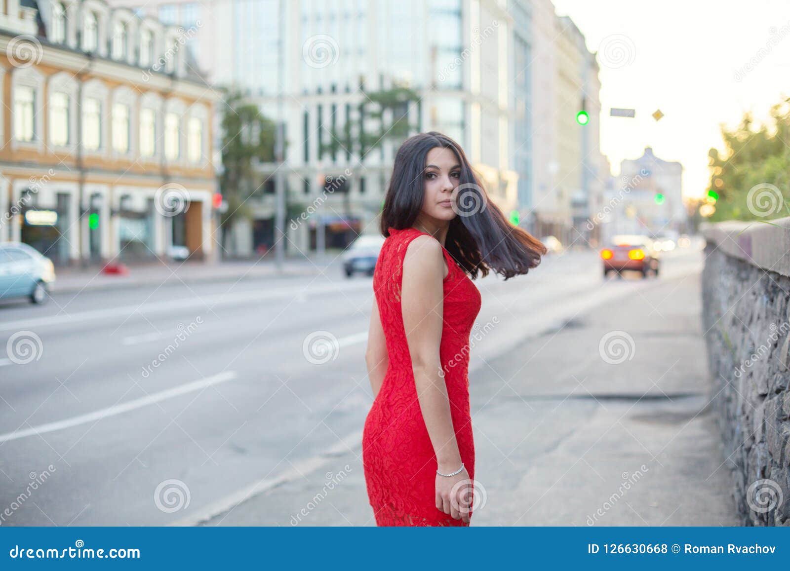 Beautiful Girl In A Red Dress Is Standing Near Of The Roadway Stock