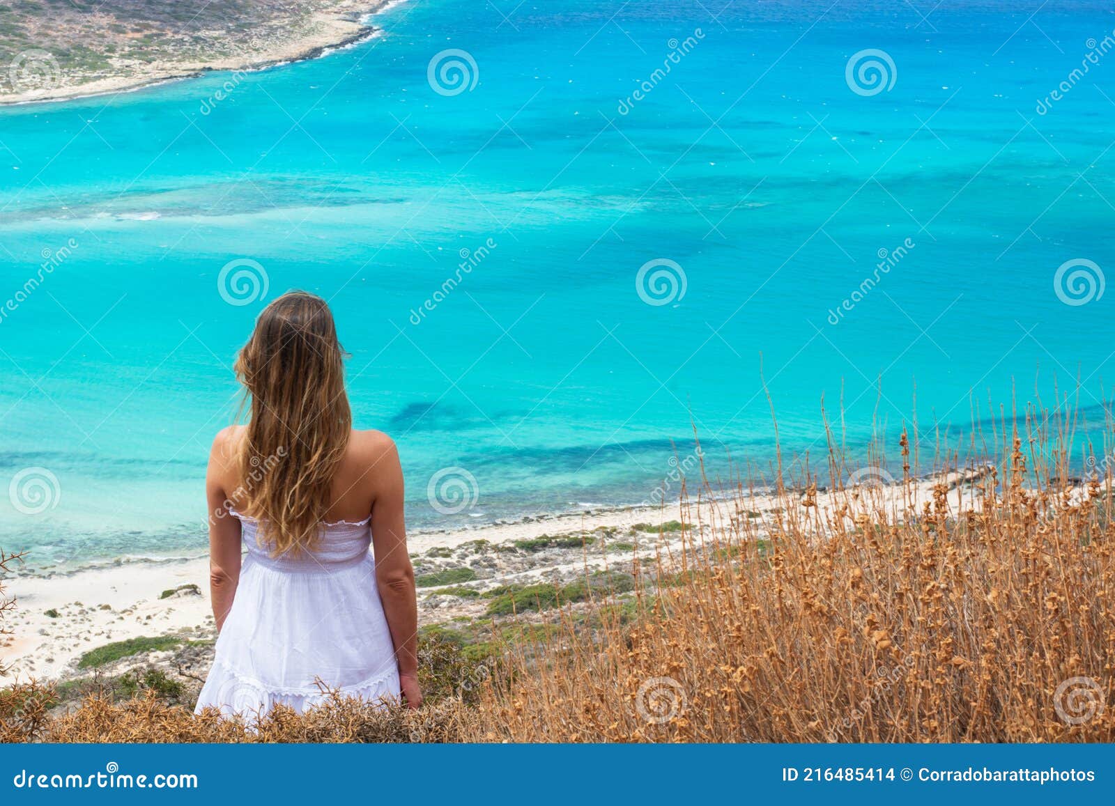 the beautiful girl in the white dress looks spellbound at the spectacular turquoise sea lagoon