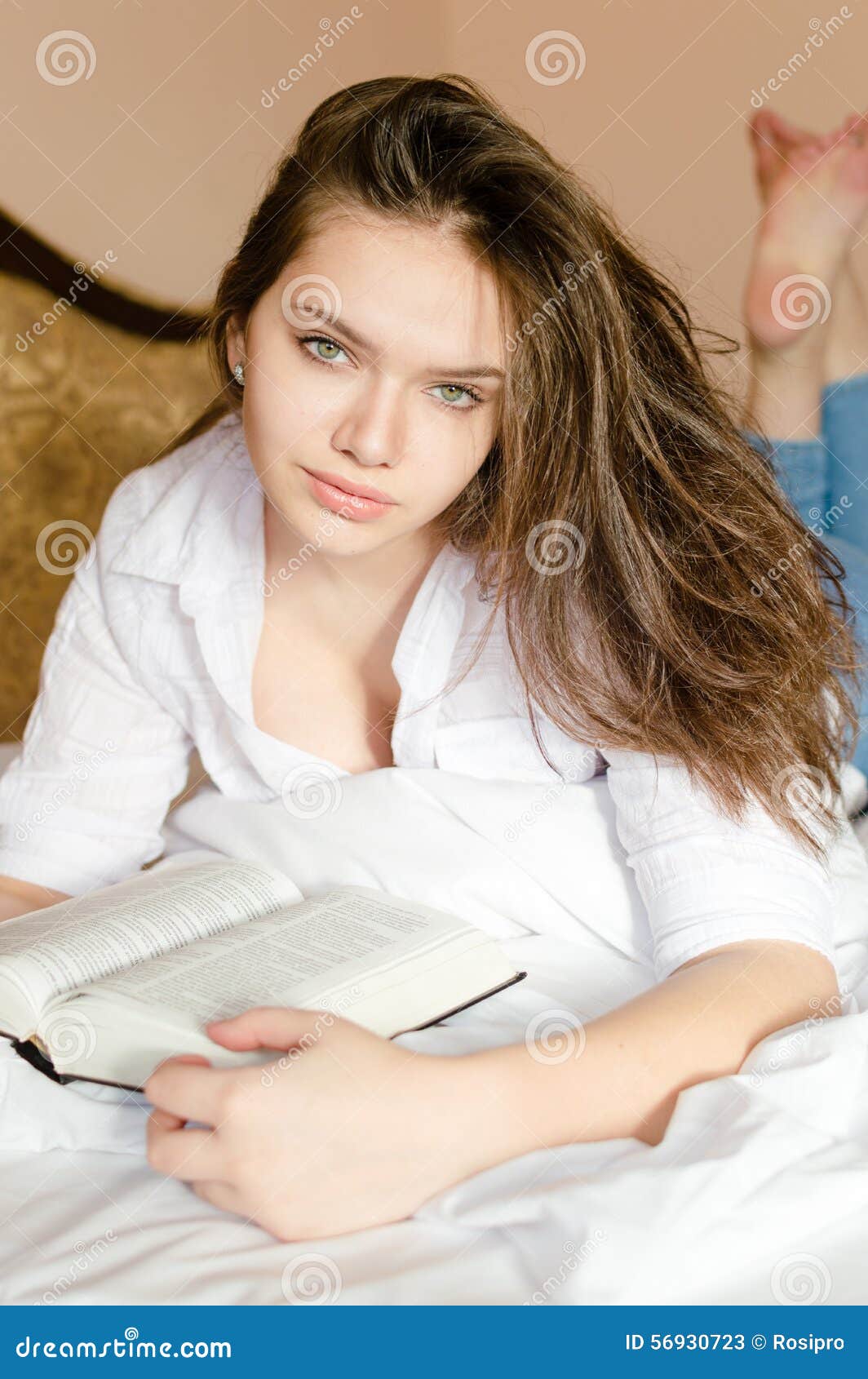 Beautiful Girl In White Shirt Lying On Bed Reading Stock