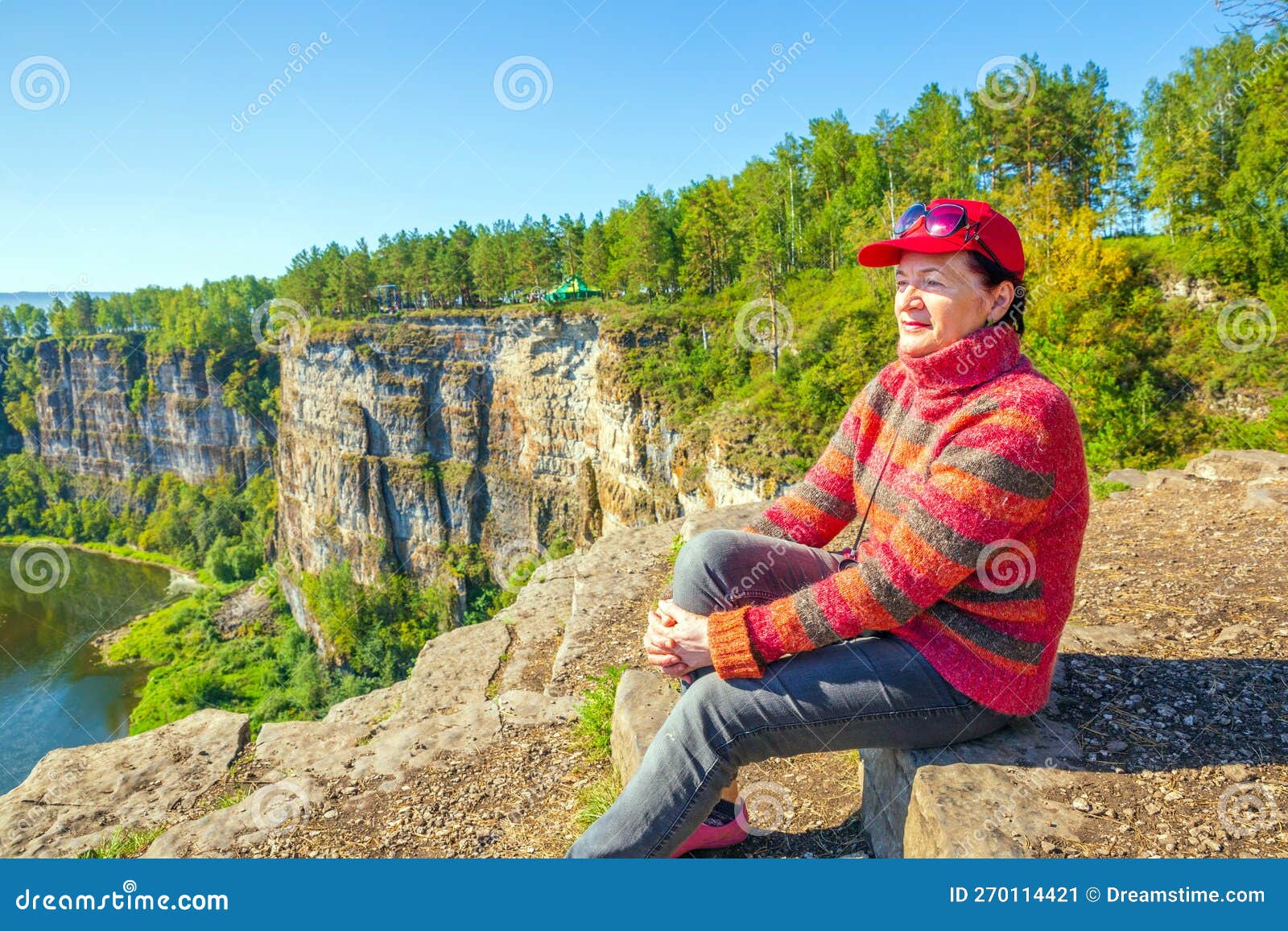 Beautiful Mature Women Sits On A High Rock Above The River And Admires The Big Aisian Cliffs