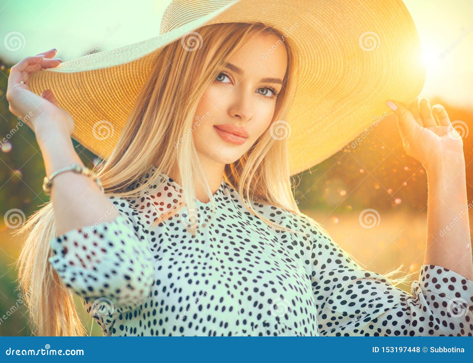 beautiful model girl posing on a field, enjoying nature outdoors in wide brimmed straw hat. beauty blonde young woman