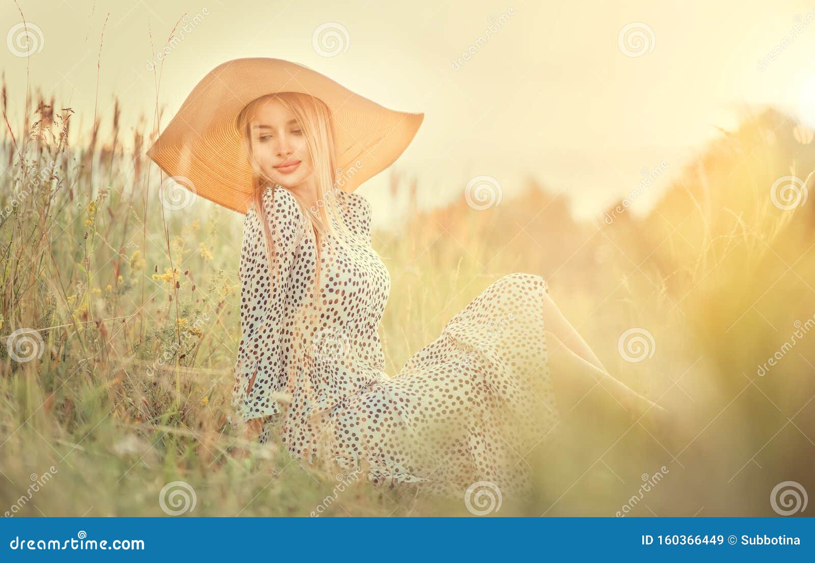 beautiful model girl posing on a field, enjoying nature outdoors in wide brimmed straw hat