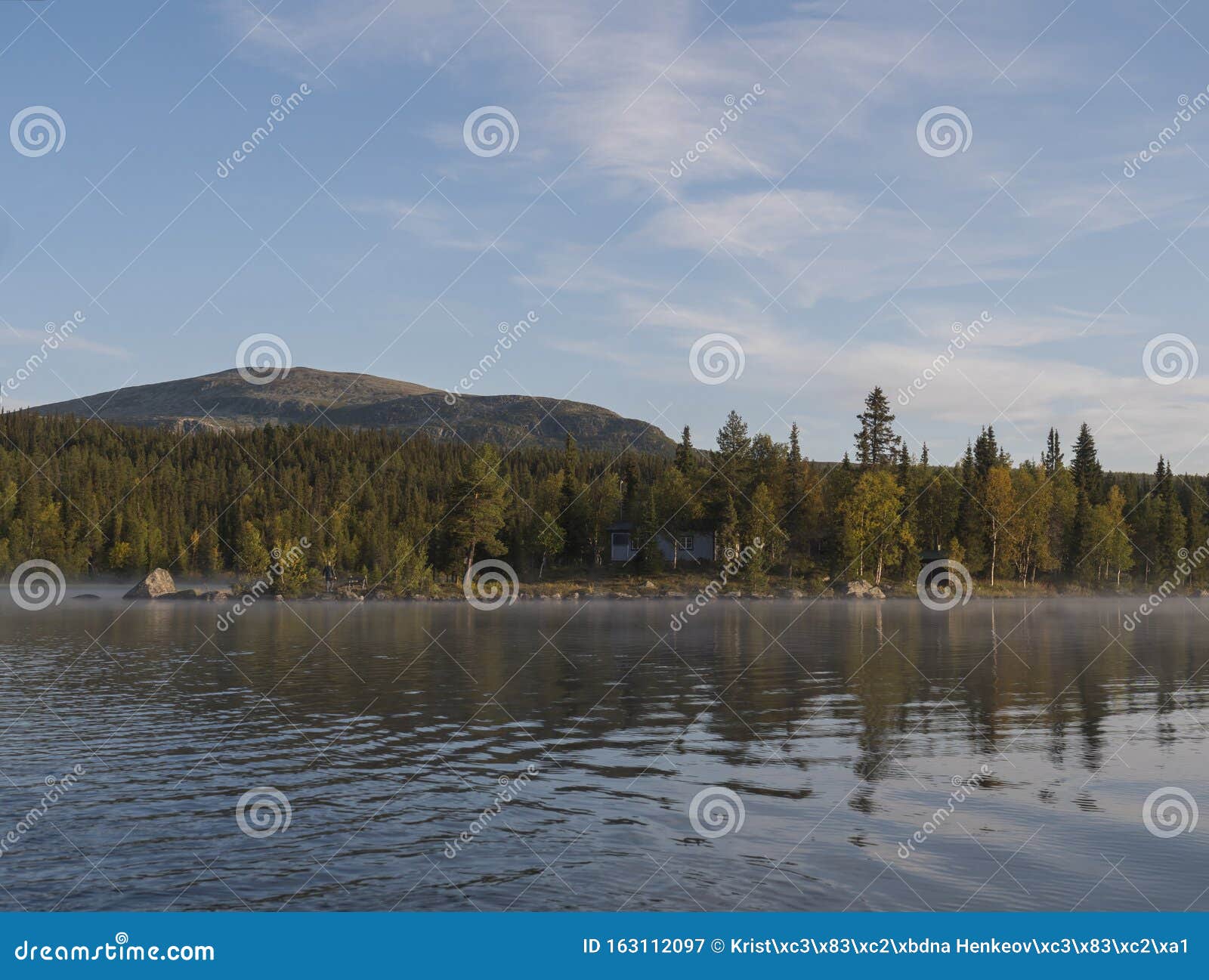 beautiful morning over lake sjabatjakjaure with view on parte fjallstuga stf mountain cabin, green hills and birch trees. sweden