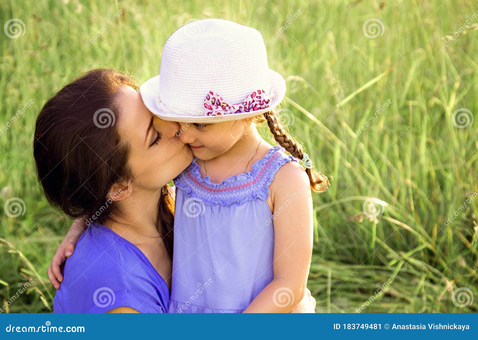 Beautiful Mother Hugging And Kissing Her Cute Small Daughter On Summer Green Grass Background 