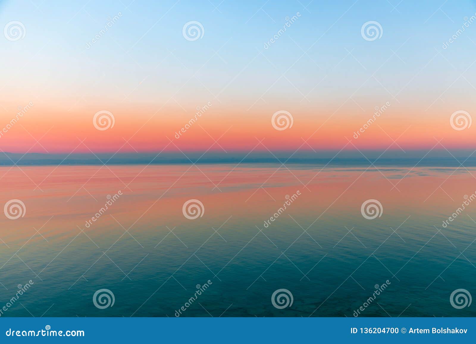 beautiful multicolor sunset reflected in the waters of lake garda, italy. skyline. visible coastline in the evening fog. winter
