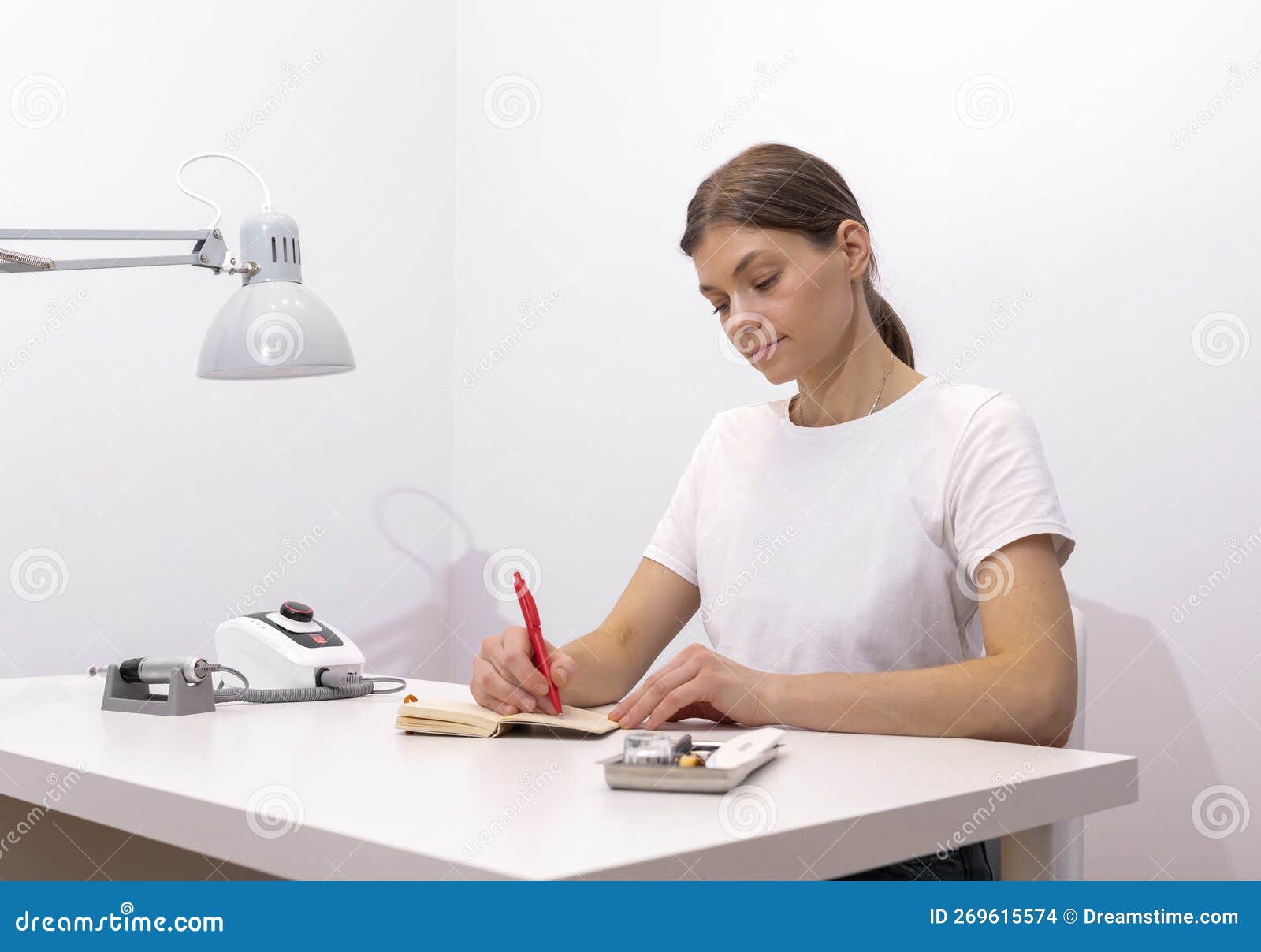 beautiful nail beautician makes notes in notebook with pen, sitting at workstation