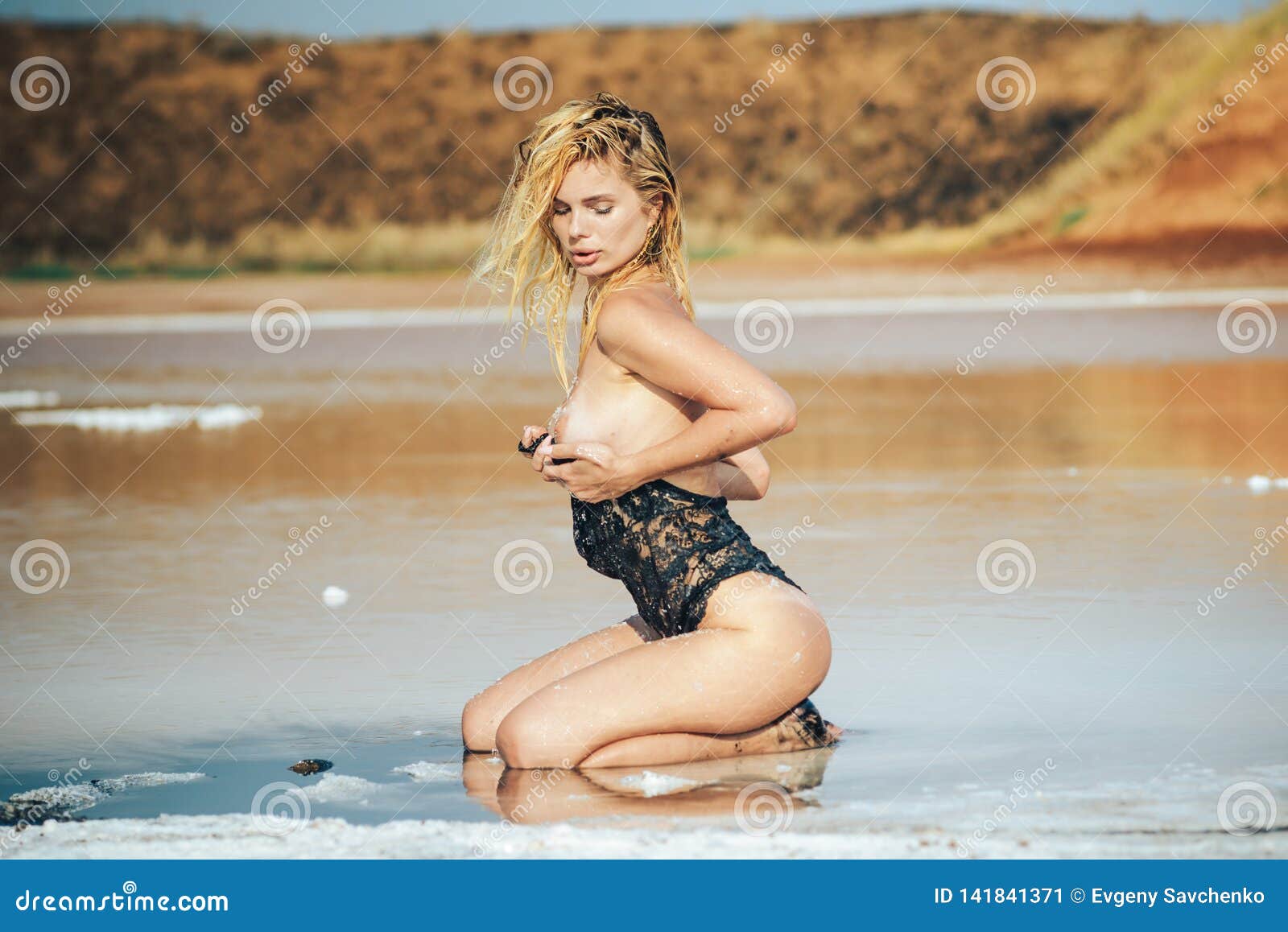 Beautiful naked girl in a mud bath. An attractive girl with a sports figure, on a deserted salt lake, bared her Breasts sunbathing and taking Spa treatments smearing the body with salt.