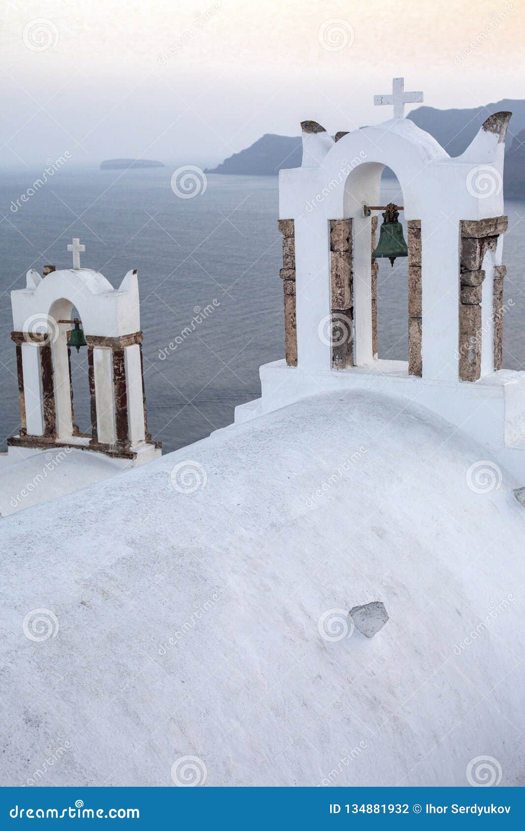 arch with a bell, white houses and church with blue domes in oia or ia at golden sunset, island santorini, greece. - immagine