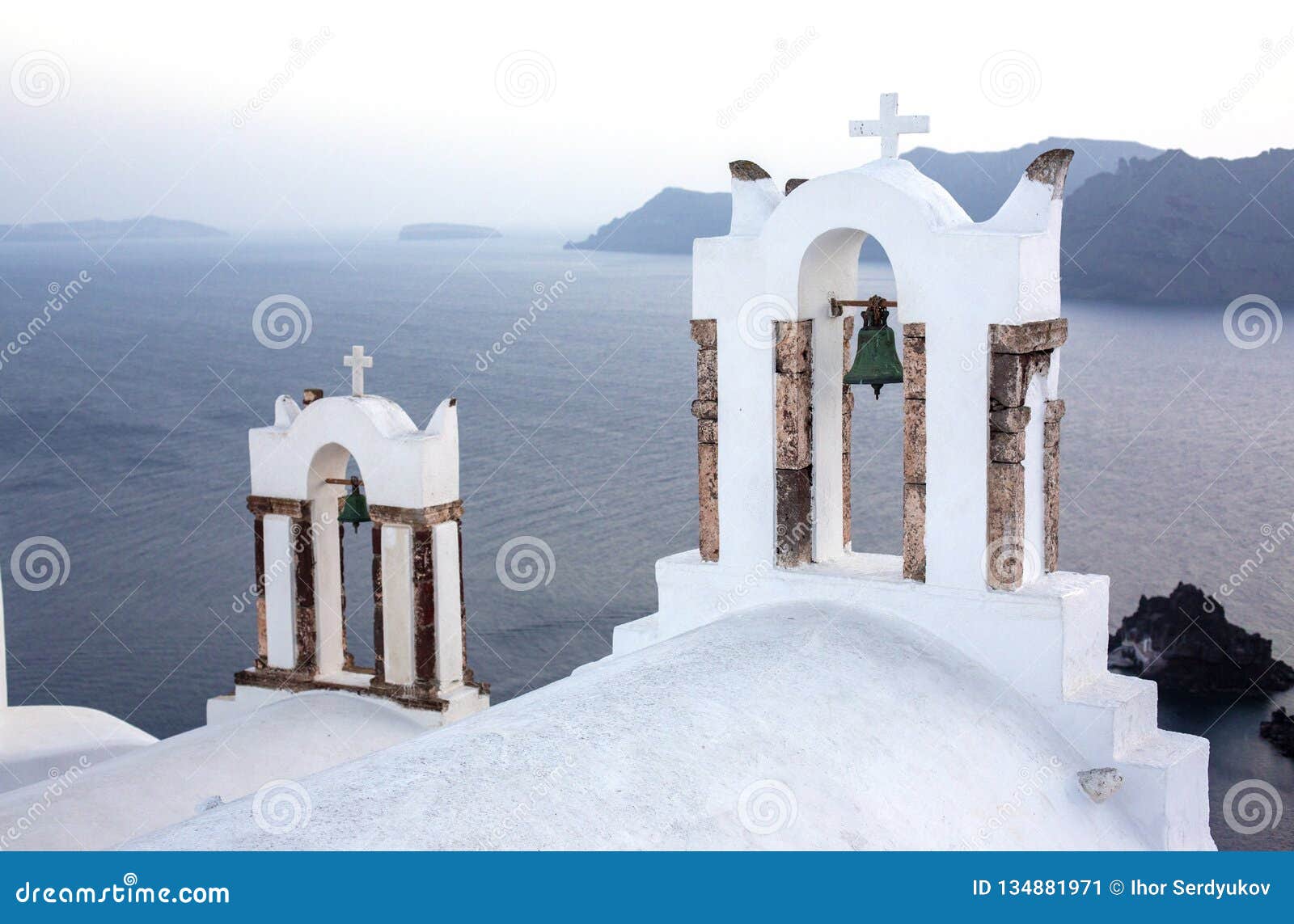 arch with a bell, white houses and church with blue domes in oia or ia at golden sunset, island santorini, greece. - immagine