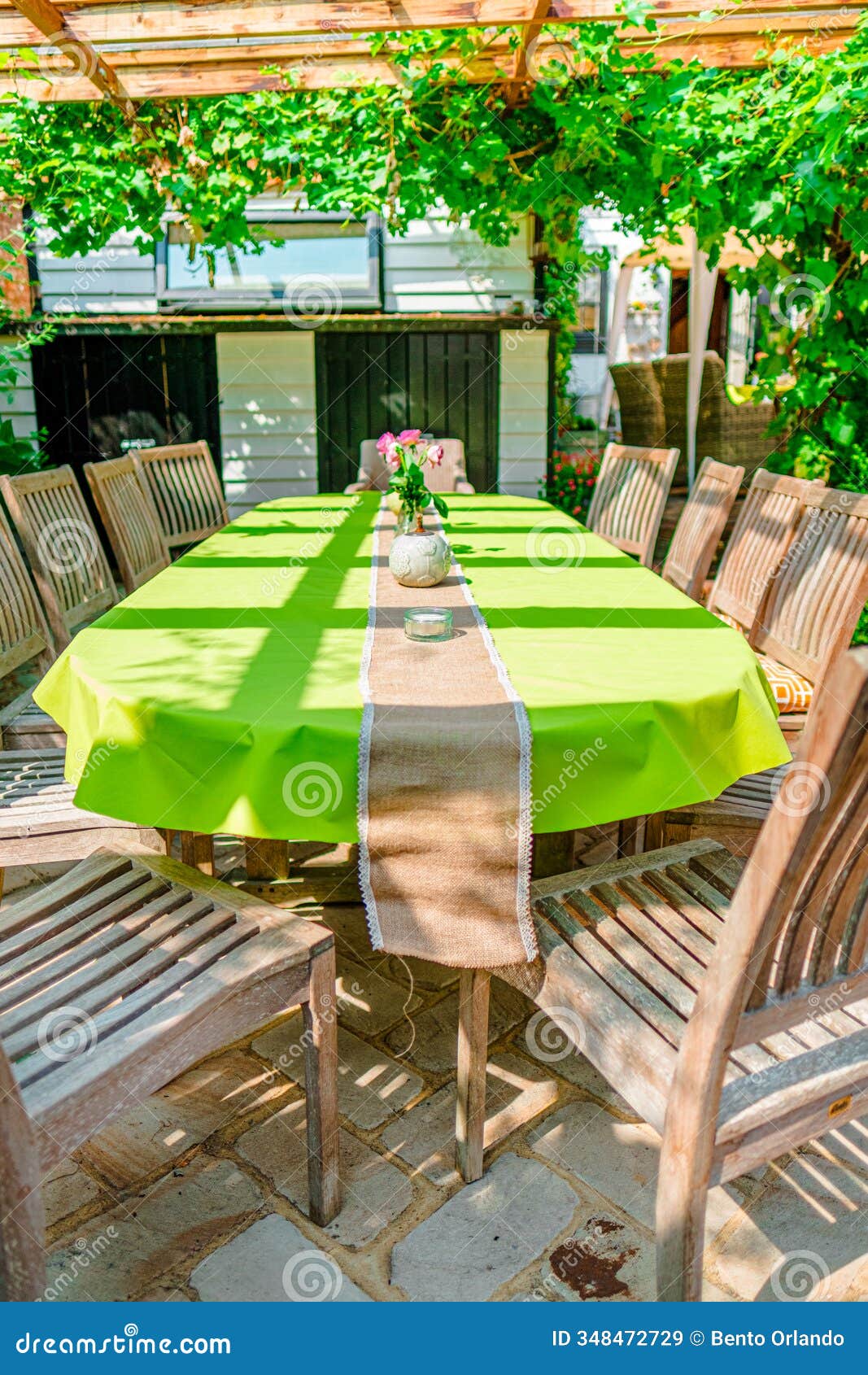 beautiful outdoor patio dining area with green tablecloth and wooden chairs under pergola with greenery, inviting for a garden