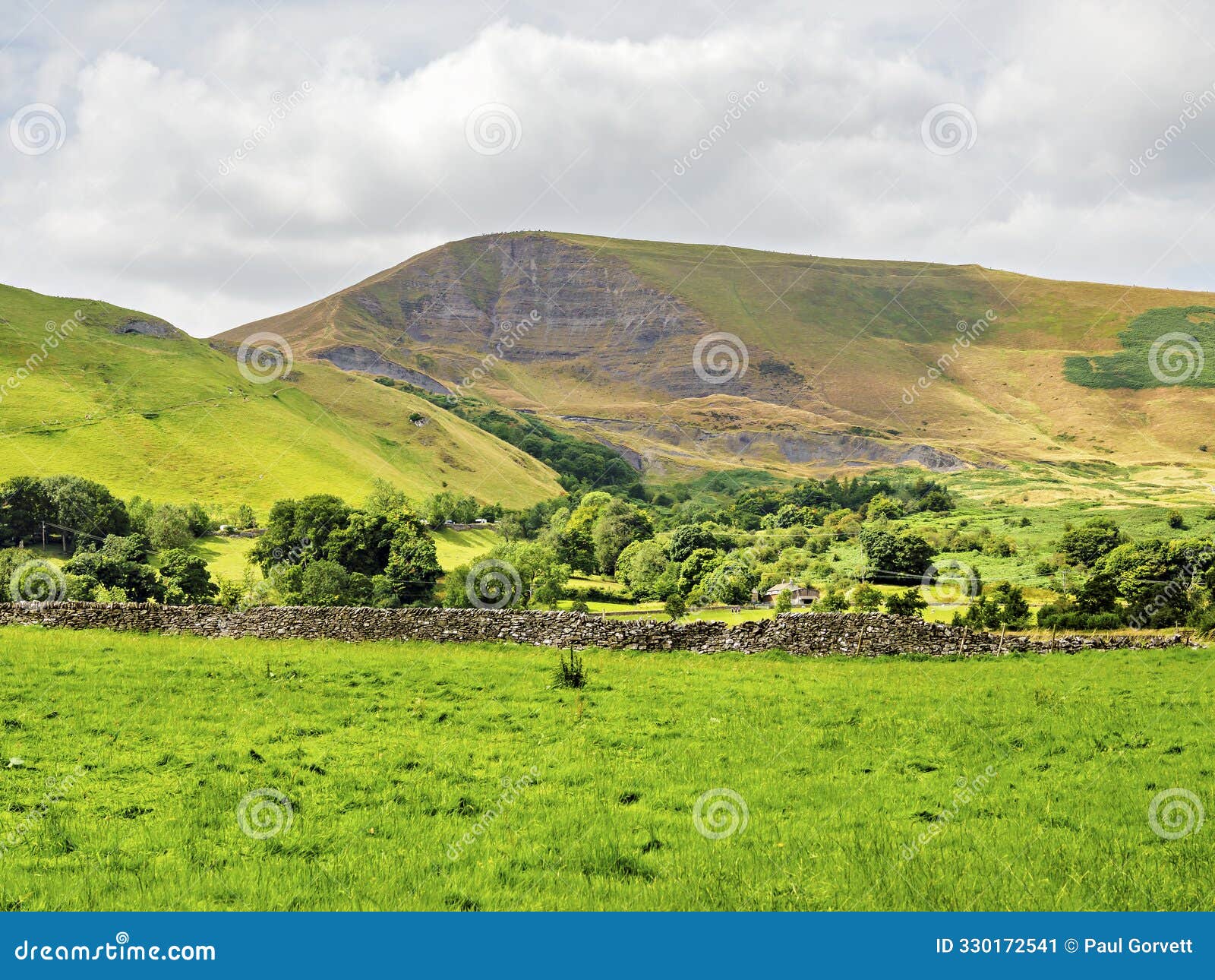 beautiful pastoral landscape with rolling green hills and a stone wall under a partly cloudy sky