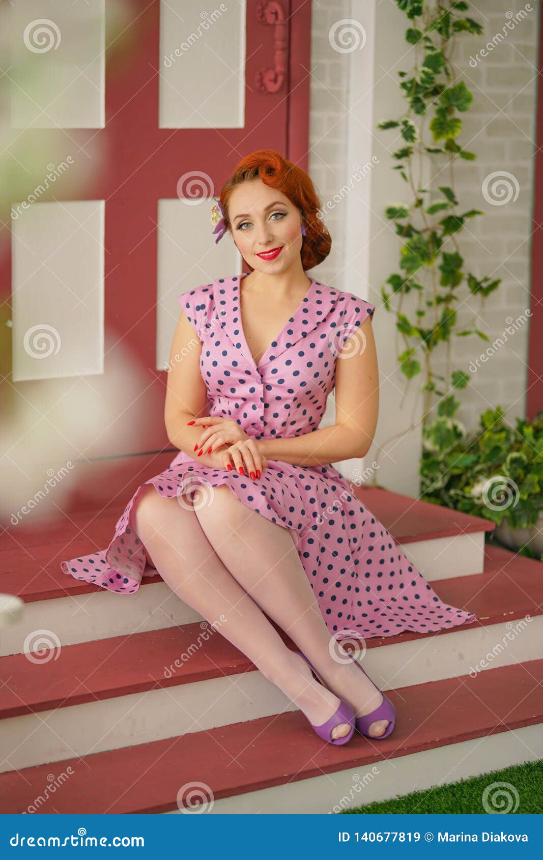 Beautiful Redheaded Pin Up Girl In Pink Polka Dot Dress And Vintage Stockings Posing Near The