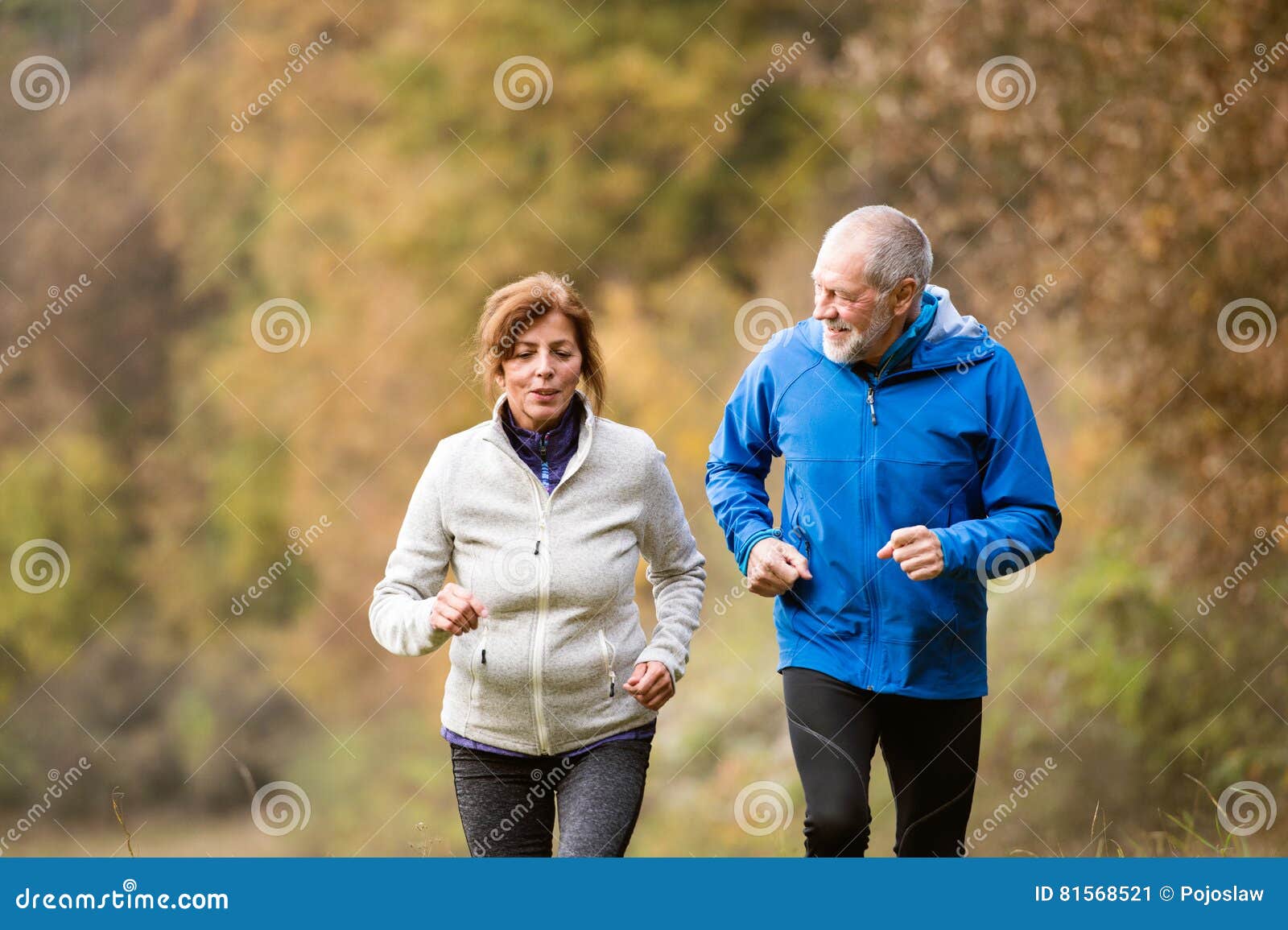 beautiful senior couple running outside in sunny autumn forest