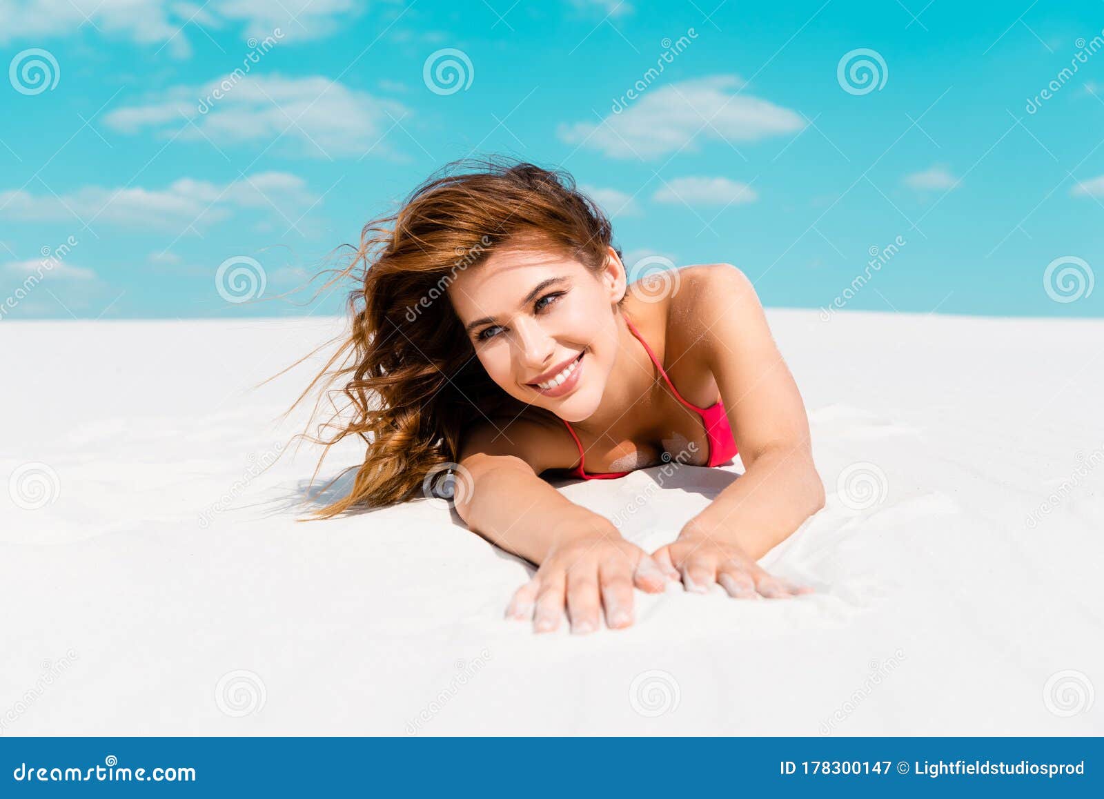 Beautiful Girl In Swimsuit Lying On Sandy Beach With Blue Sky And Clouds At Background Stock