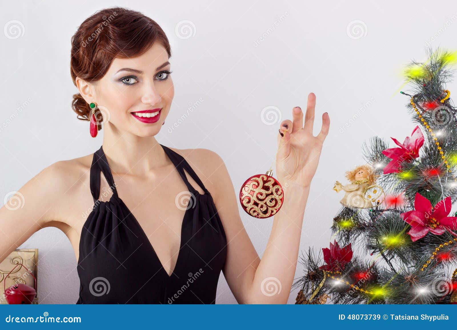 Beautiful happy smiling young woman in evening dress with bright makeup with red lipstick, decorates a Christmas tree for the new year