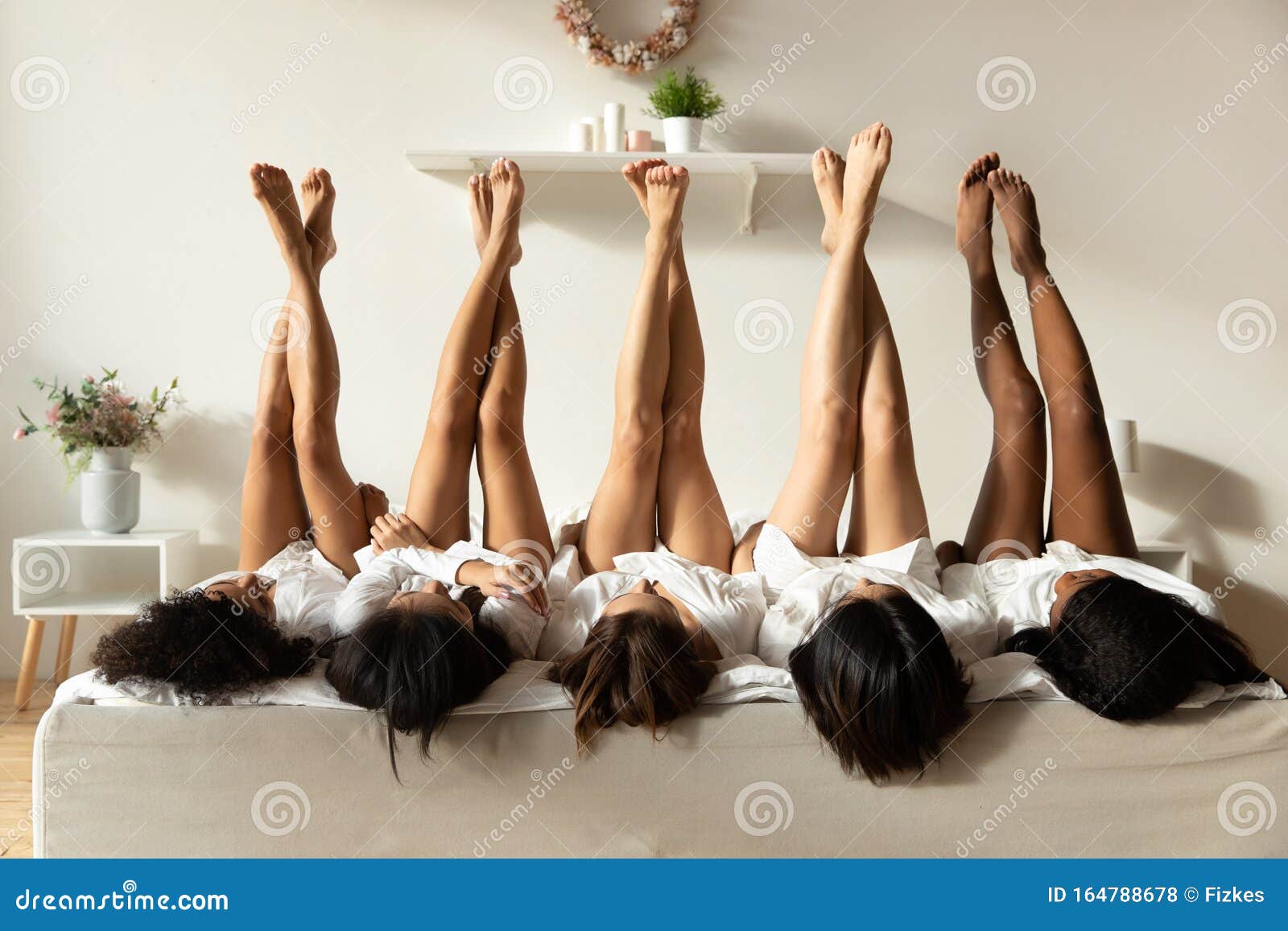 beautiful sexy multiethnic girls lying on bed raise legs up