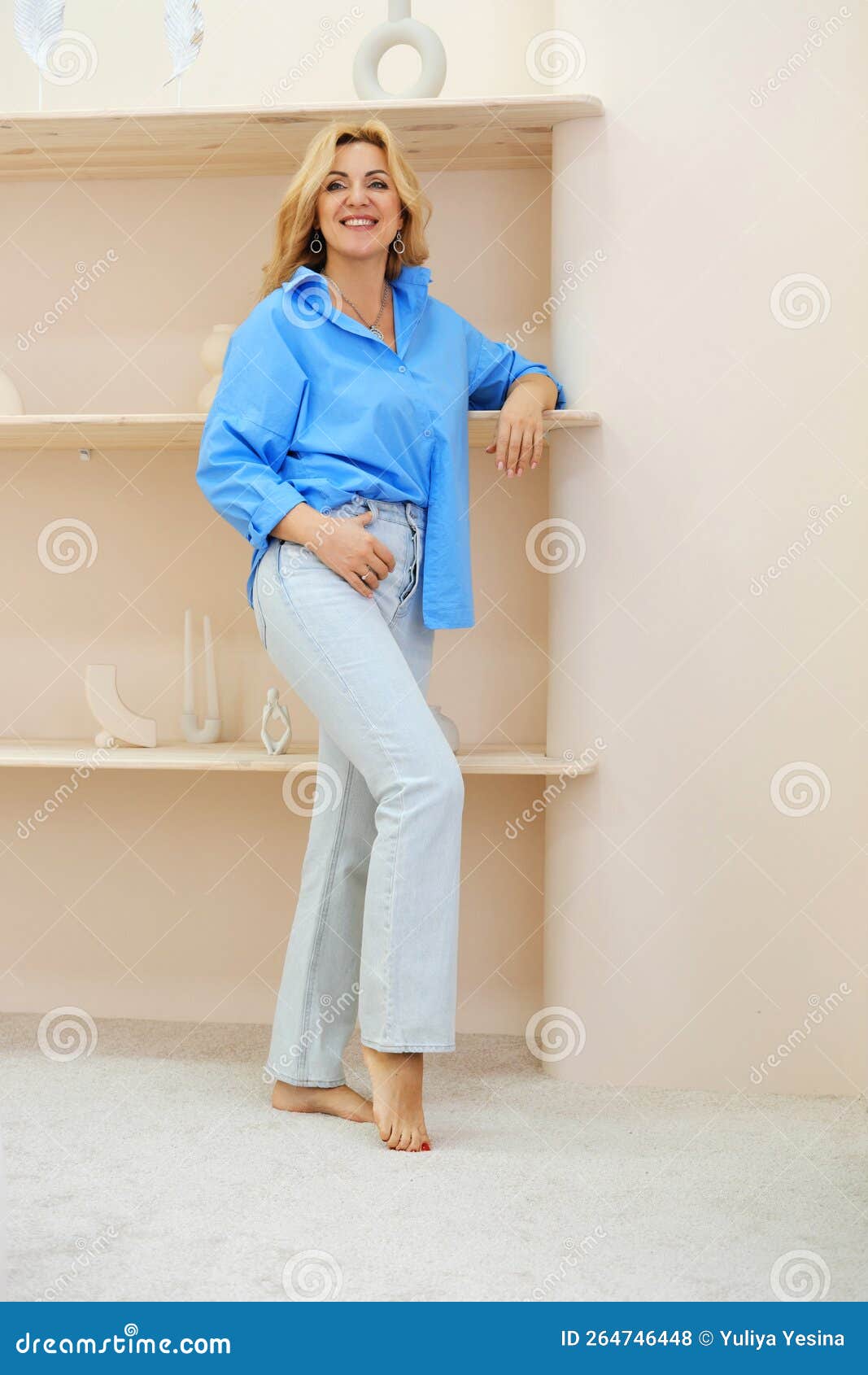Beautiful Slim Mature Blonde Woman in a Blue Shirt and Jeans Posing in a  Beige Interior and Smiling Stock Photo - Image of attractive, fashion:  264746448